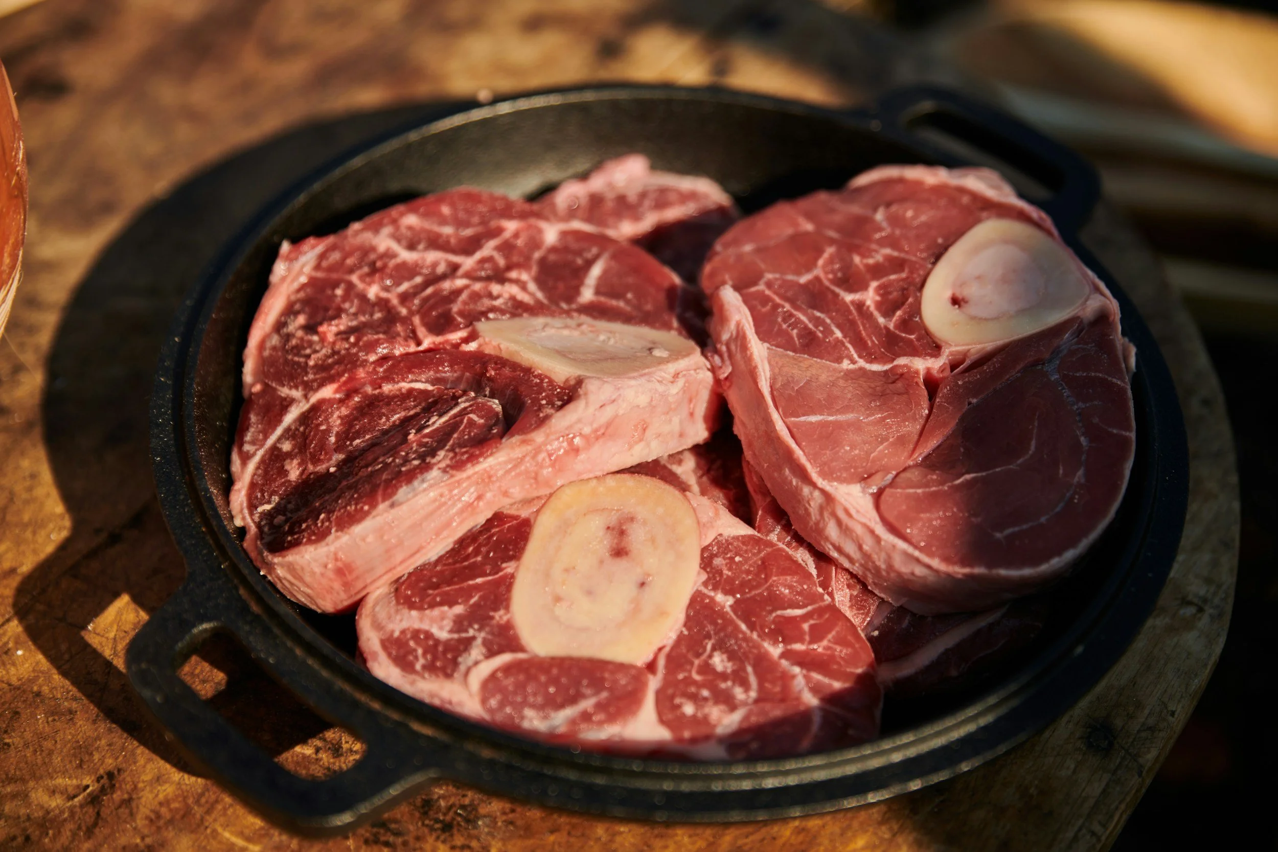 Raw bone-in beef steaks with marrow bones on a cast iron skillet on a wooden surface.