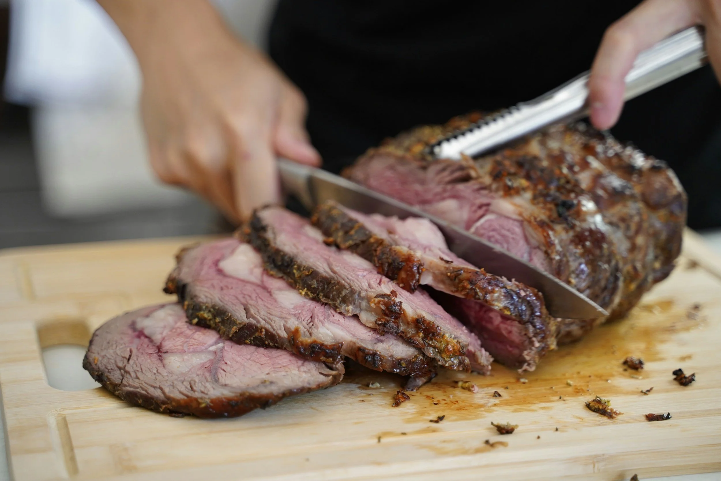 Person slicing cooked roast beef on a wooden cutting board.