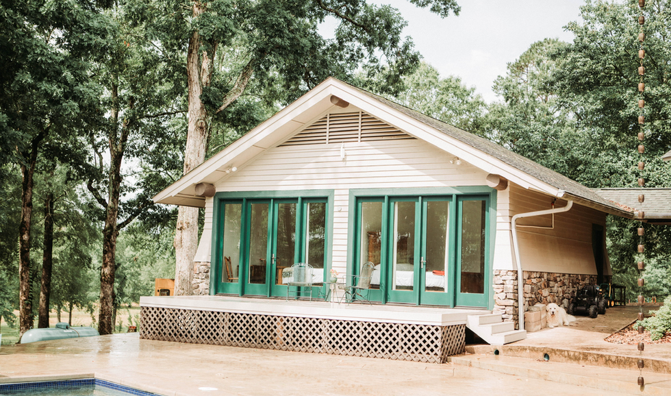 A house with a large glass sliding door patio, surrounded by trees, and a dog lying on the ground near the house.