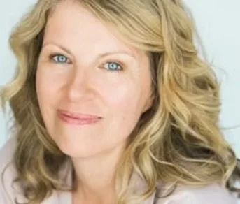 Close-up of a woman with blonde curly hair and blue eyes, smiling gently