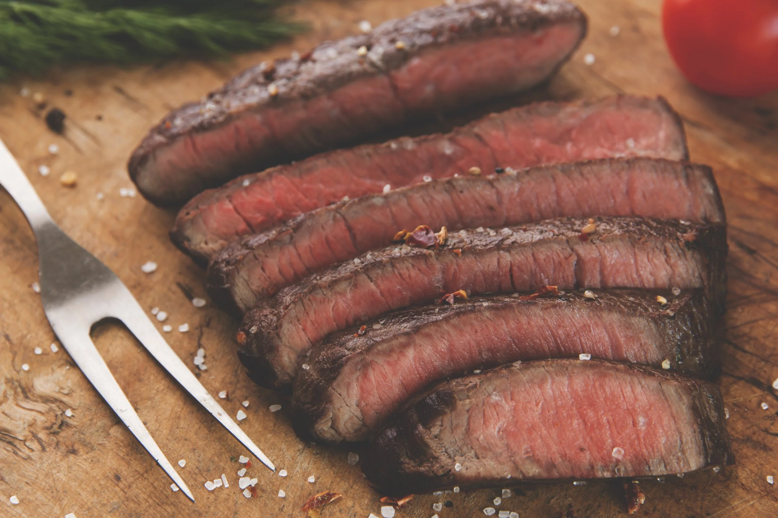 Sliced medium-rare steak on a wooden cutting board with coarse salt and a fork nearby.