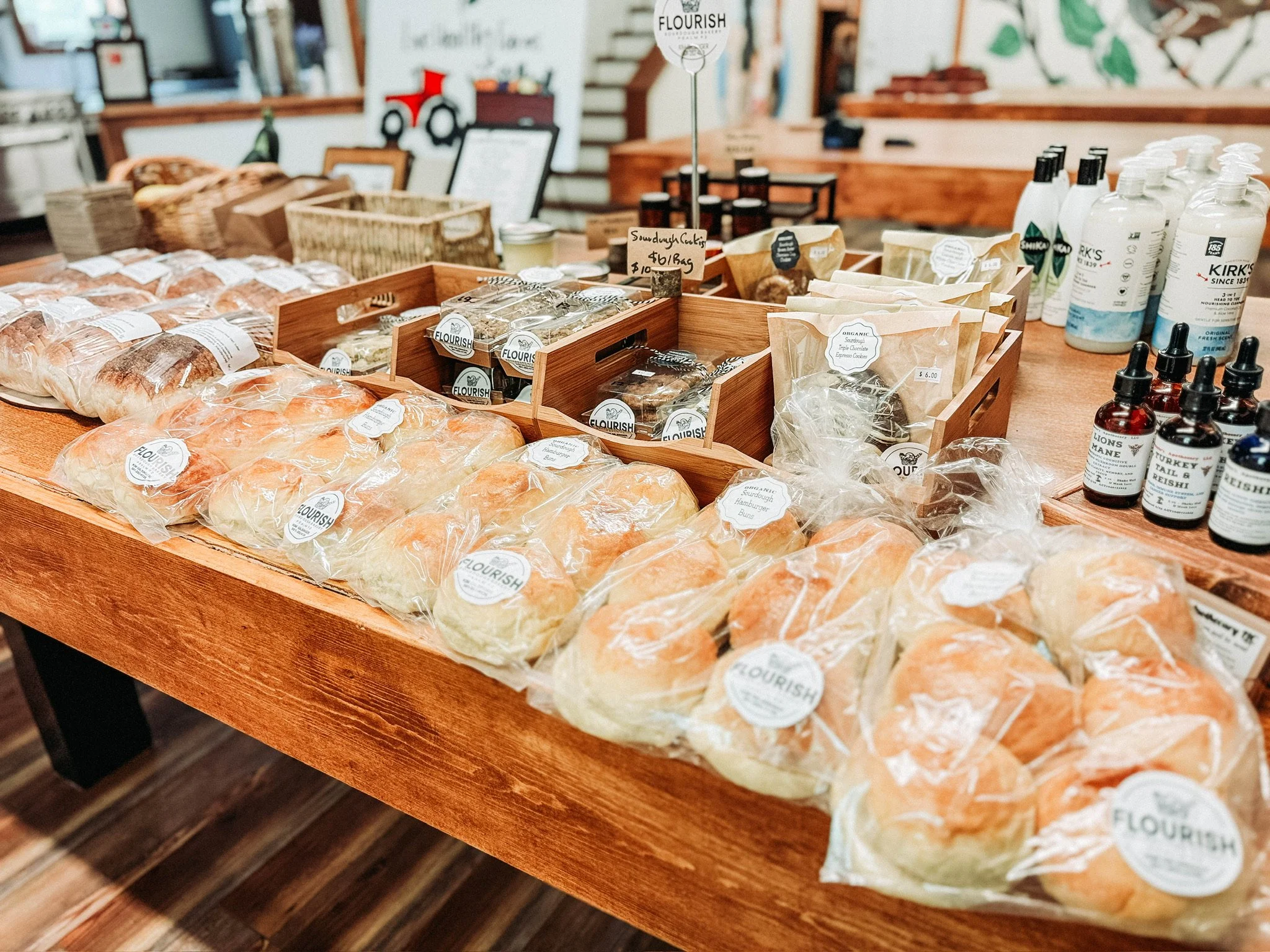 A display of bagged bread rolls, various baked goods, and packaged products on a wooden table at a bakery or specialty shop. Live Healthy Farms - Hot Springs, AR