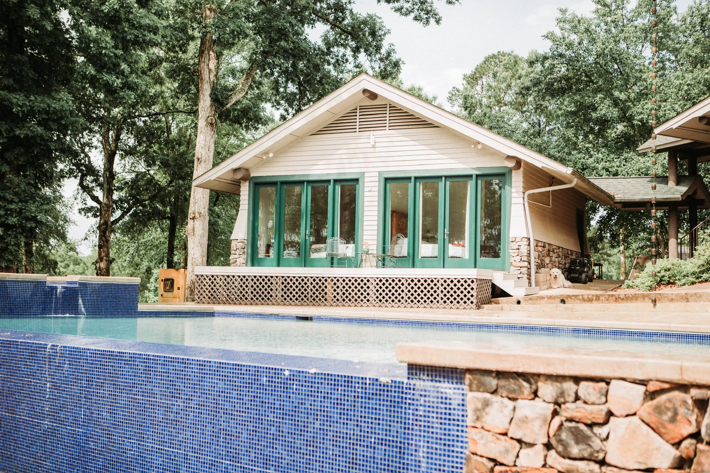 A house with large glass sliding doors, situated near a swimming pool with blue mosaic tiles, surrounded by trees. AIRBNB Live Healthy Farms - Hot Springs, AR