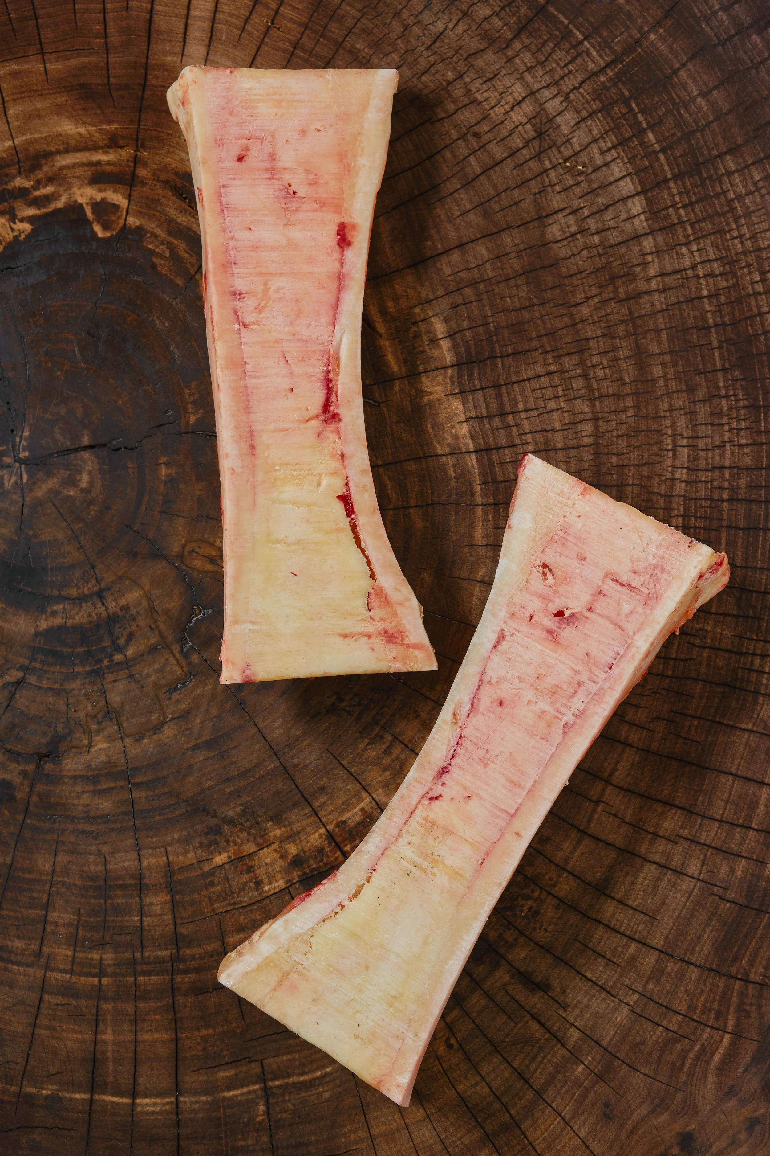 Two pieces of raw beef rib bones on a wooden surface.