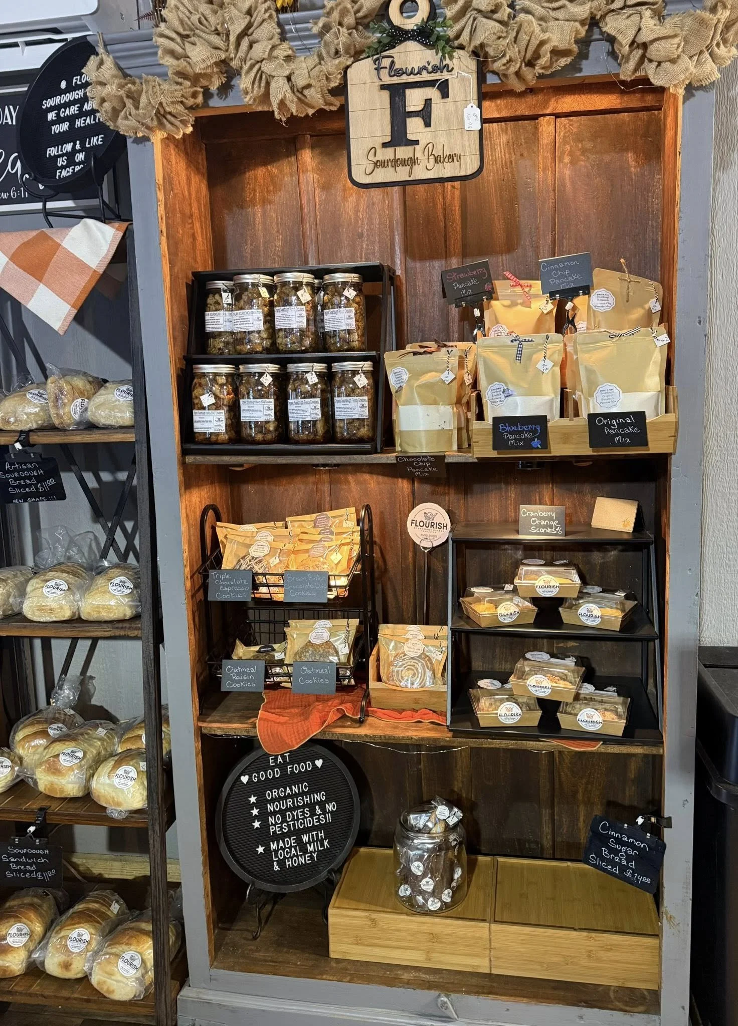 Display of baked goods and jars at Flourish Sourdough Bakery, including cookies, pancake mixes, and bread, with signage and decorative elements.
