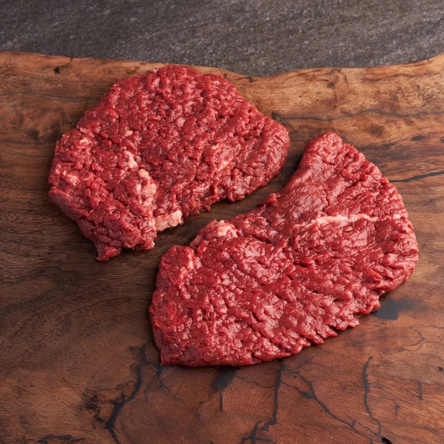 Two pieces of raw ground beef on a wooden cutting board.