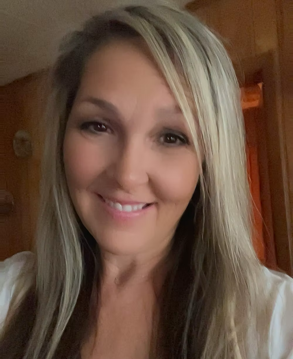 Close-up of a smiling woman with long, blonde hair and light makeup, indoors with wooden paneling in the background.  jENNY MASSAGE THERAPIST . Live Healthy Farms - Hot Springs, AR