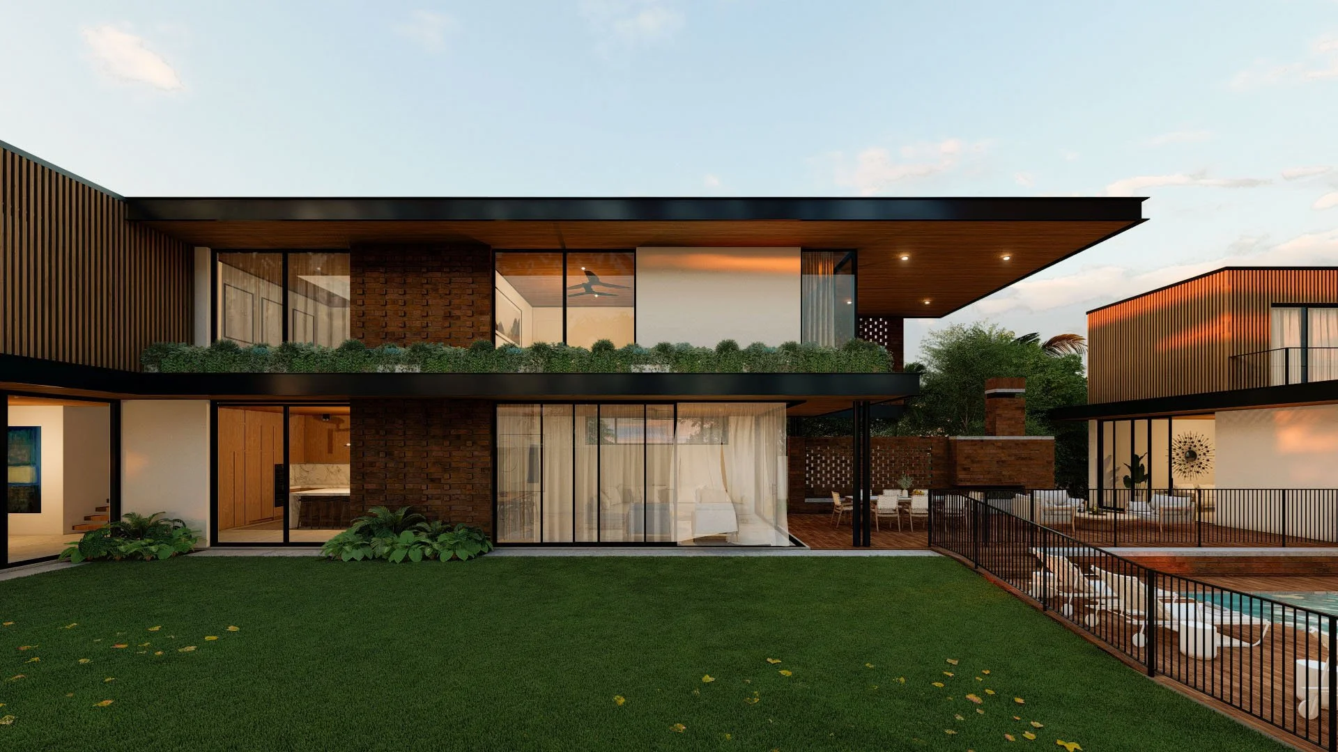 Modern two-story house with large glass windows, a green lawn, and outdoor seating area surrounded by black metal fencing. The house features wood and brick exterior with greenery on the balcony.
