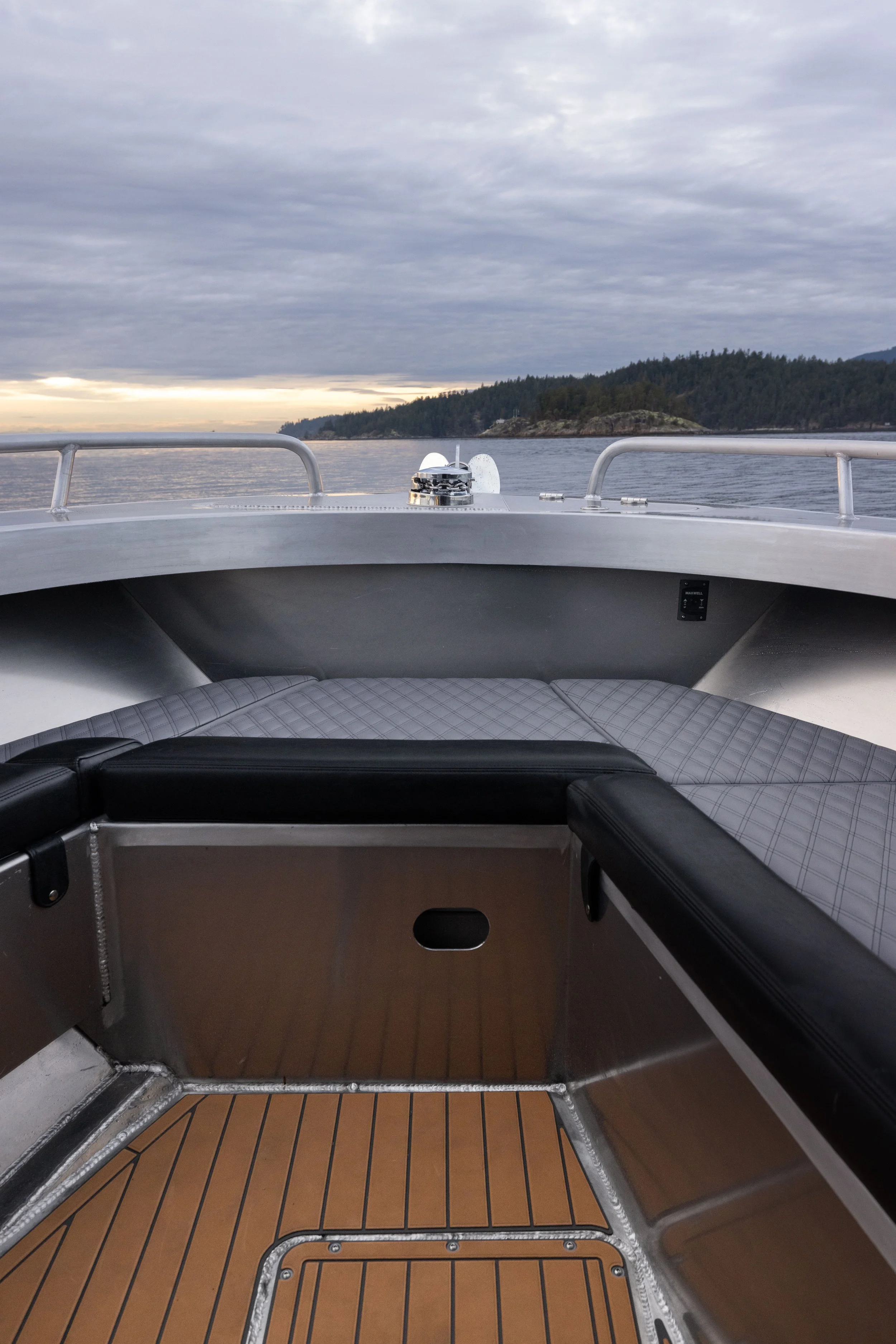 View from the bow of a boat showing a cloudy sky, water, and a distant shoreline with trees.