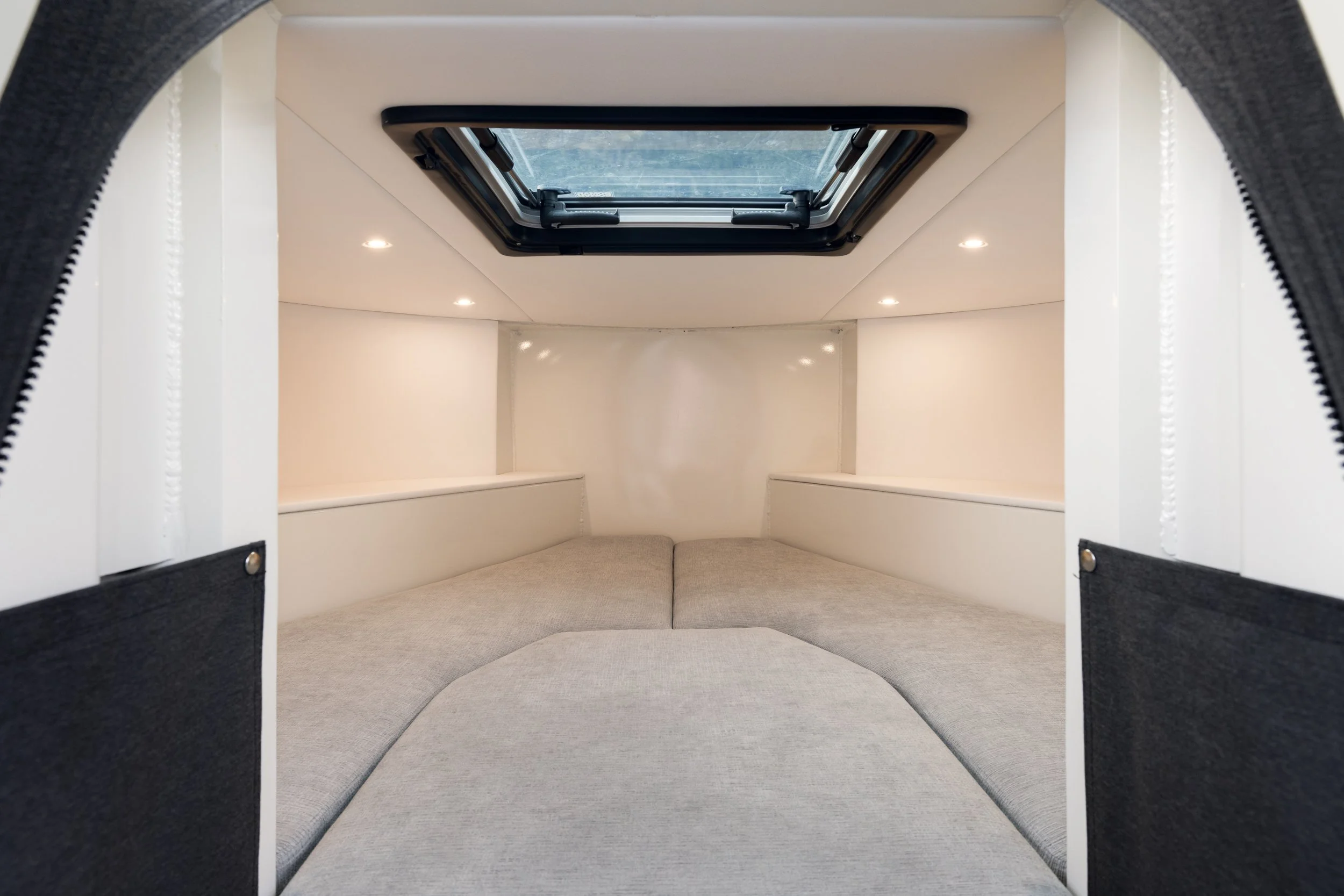 Interior of a Defender 22 storm bow with a bed space, light-colored walls, a skylight window on the ceiling, and built-in shelves.