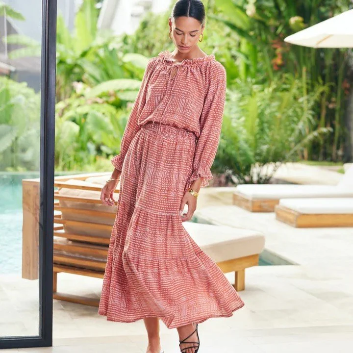 Woman in a red patterned 100% cotton maxi dress standing outdoors near a pool and greenery.