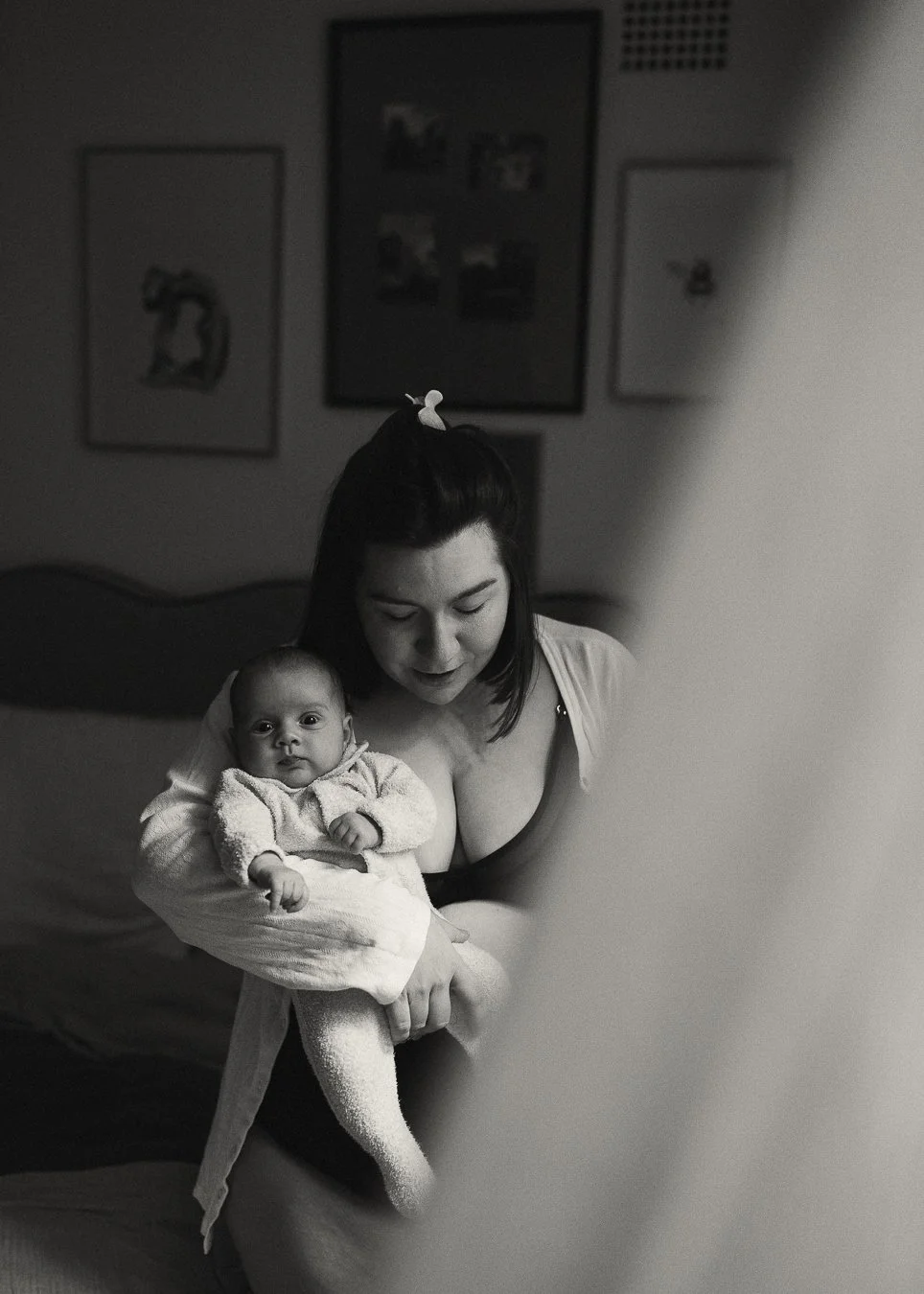 A woman holding a baby in a bedroom, both looking at the camera, in black and white.