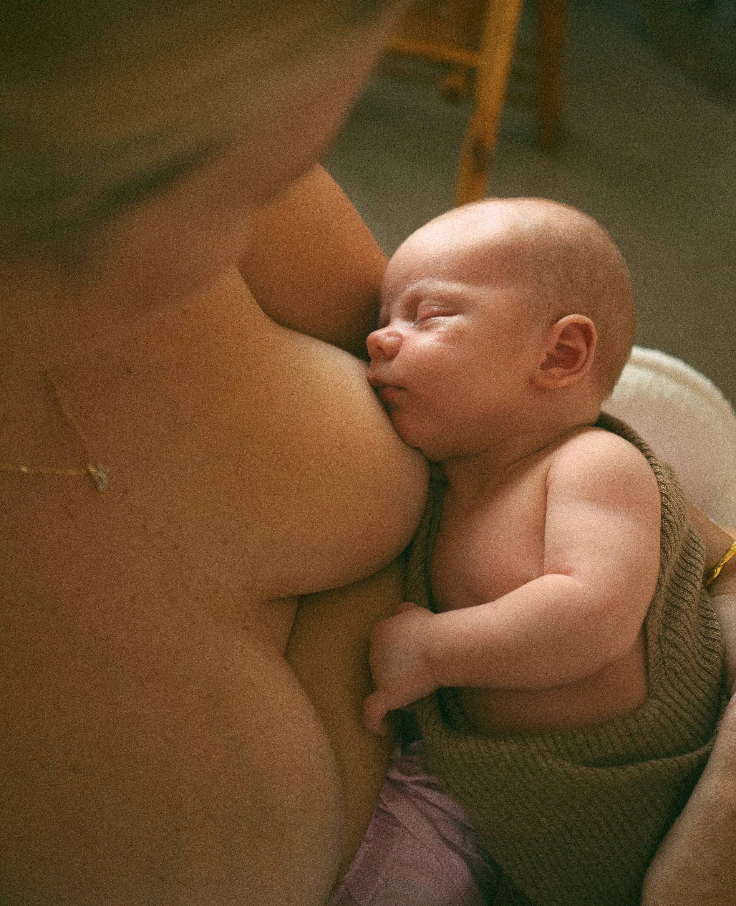 A baby breastfeeding from a mother's breast, resting peacefully with eyes closed.