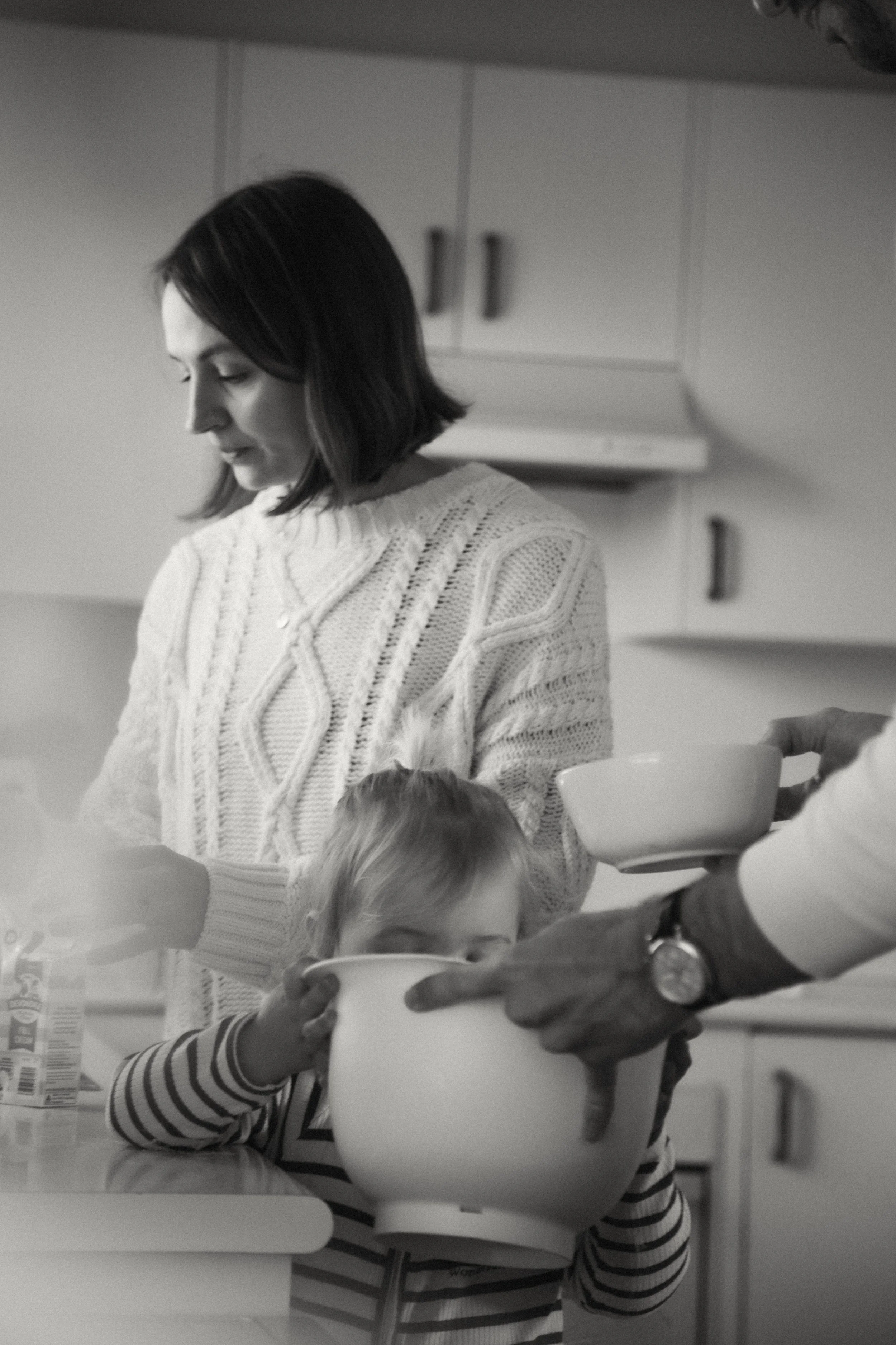 A woman and a young girl in a kitchen holding bowls and a spoon, preparing food together in black and white.
