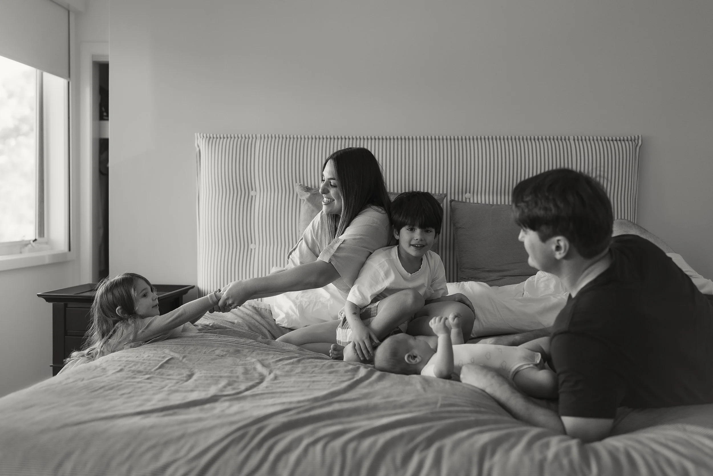 A family of five enjoying time together on a bed in a bedroom, smiling and playing with their children and each other.