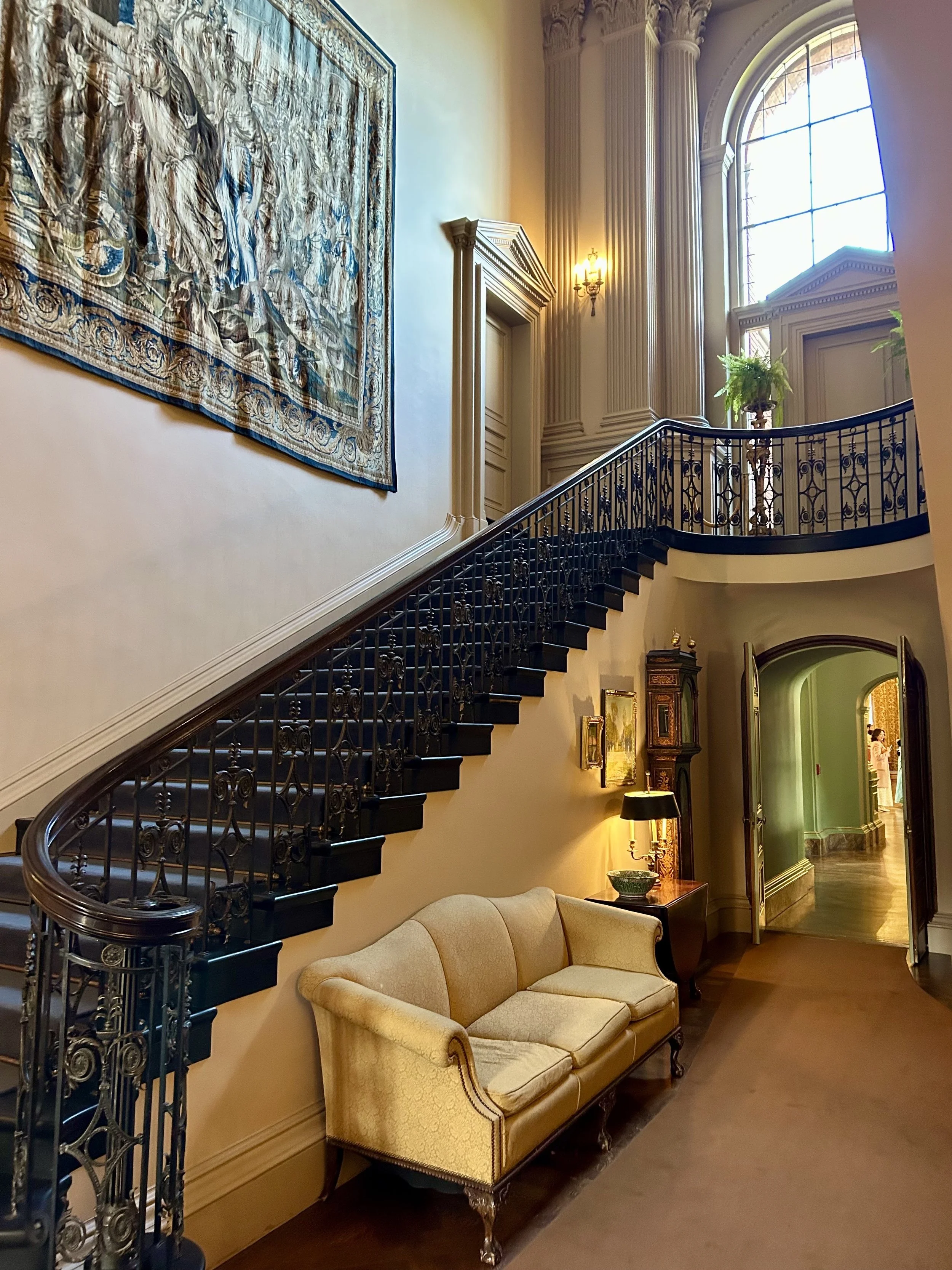 An elegant, multi-story interior space with a staircase, large window, vintage furniture, and decorative elements.