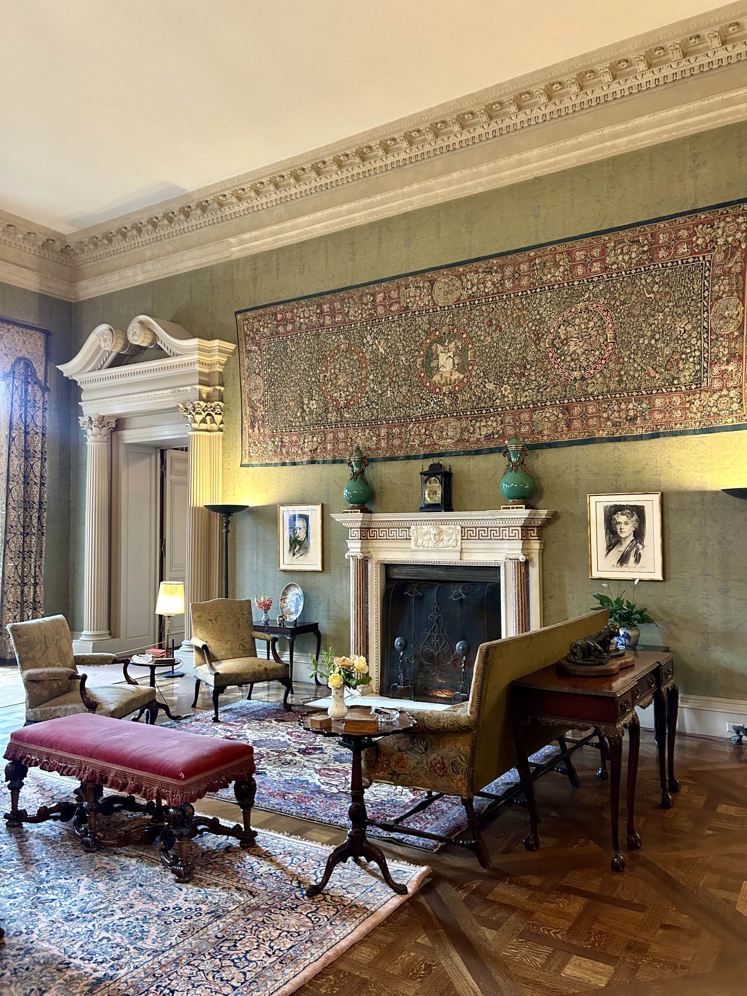 A beautifully decorated living room with antique furniture, a large ornate rug, a fireplace, and artwork on the walls.