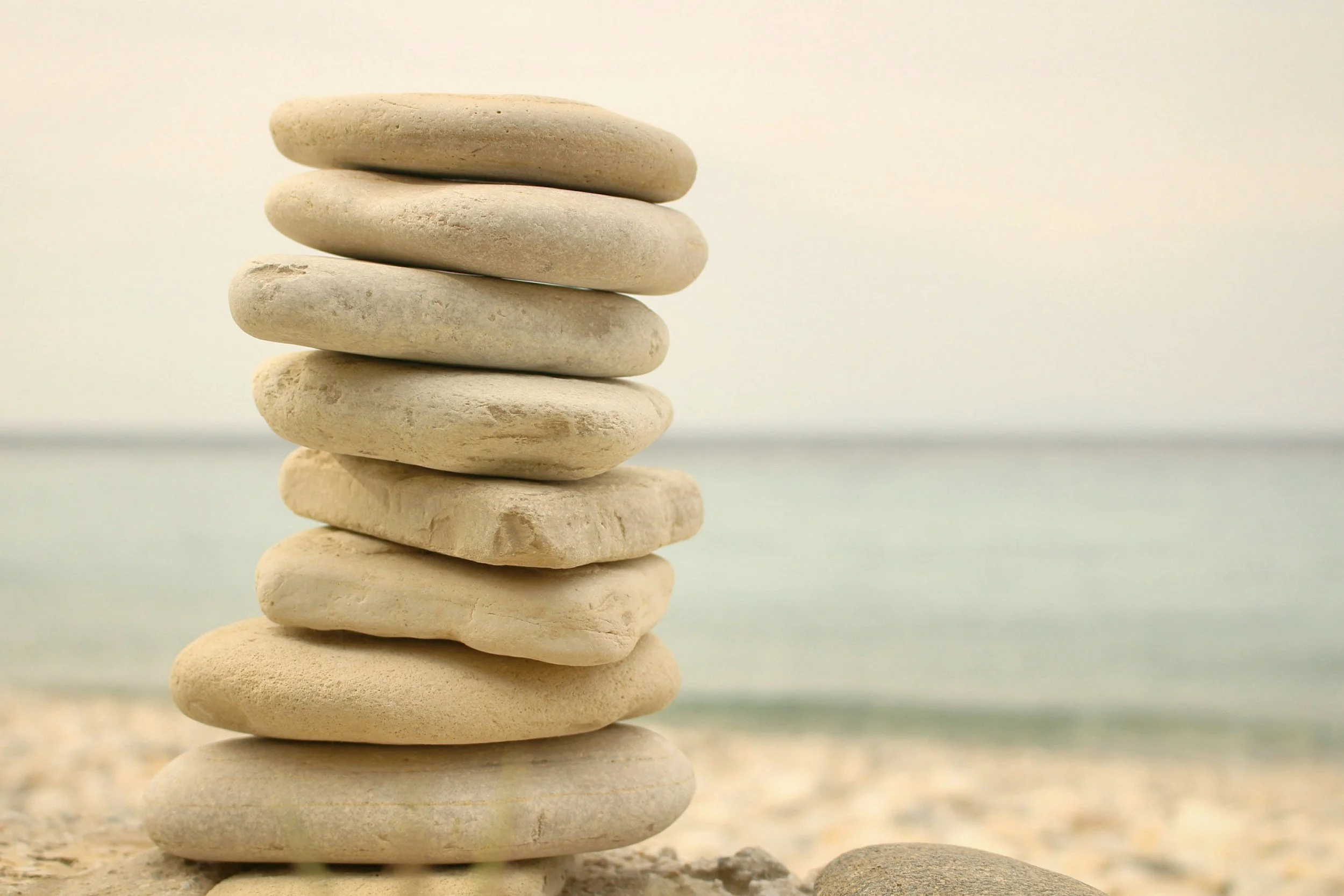 Stack of smooth, white beach stones on sandy ground near the ocean with a blurred horizon and sky in the background.