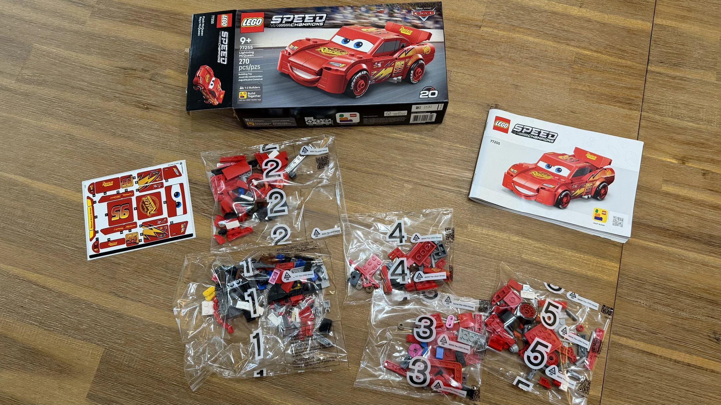 LEGO Lightning McQueen 77255 box, instructions, five numbered bags, and sticker sheet on a wooden table.