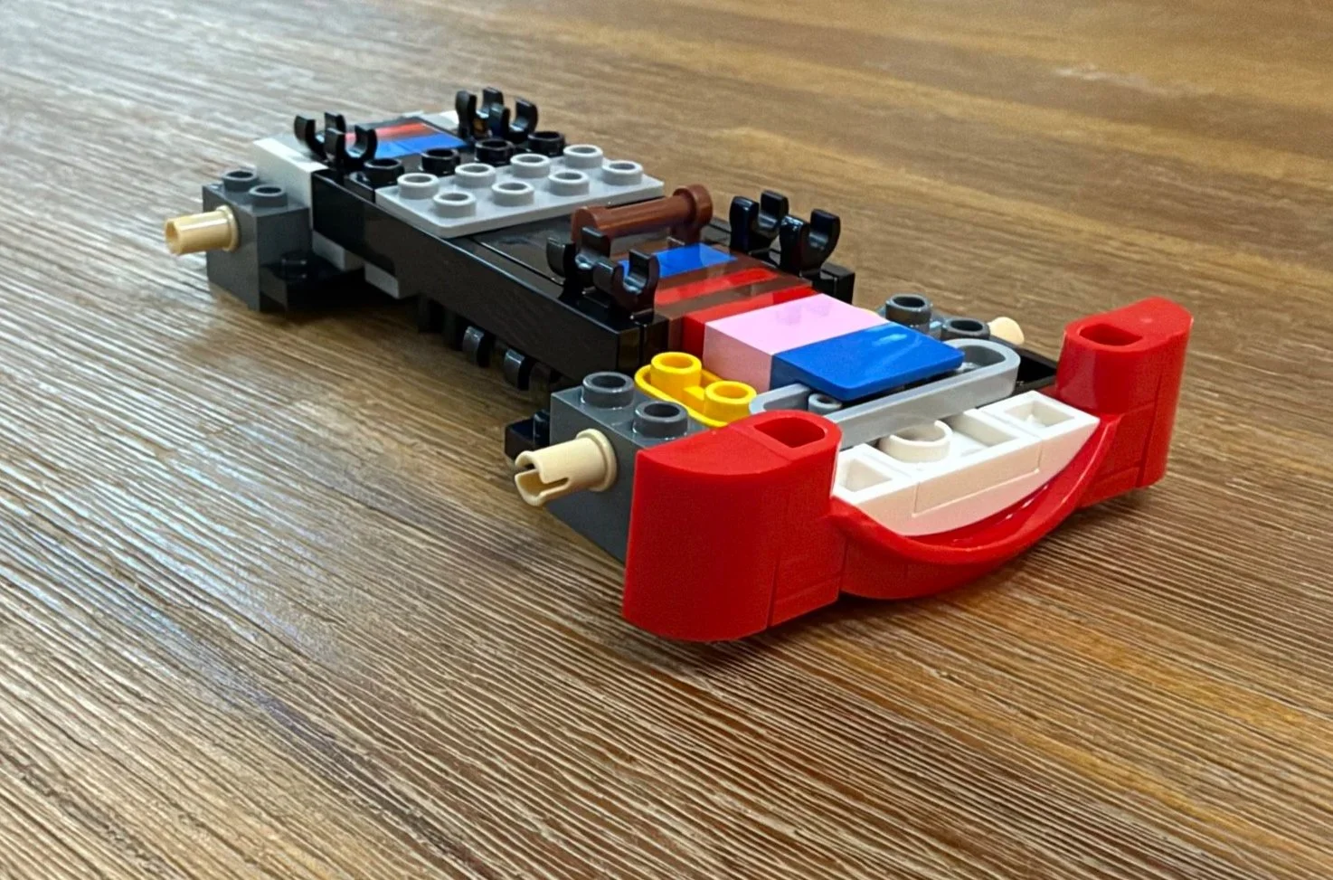 Early LEGO Lightning McQueen frame with exposed clips and axles, colorful internal pieces, and a red smiling front bumper.