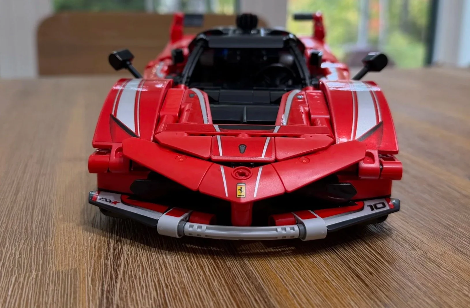 Front view of the completed Ferrari FXX K with closed hood, red and silver panels, Ferrari badge, and a curved gray lower bumper.