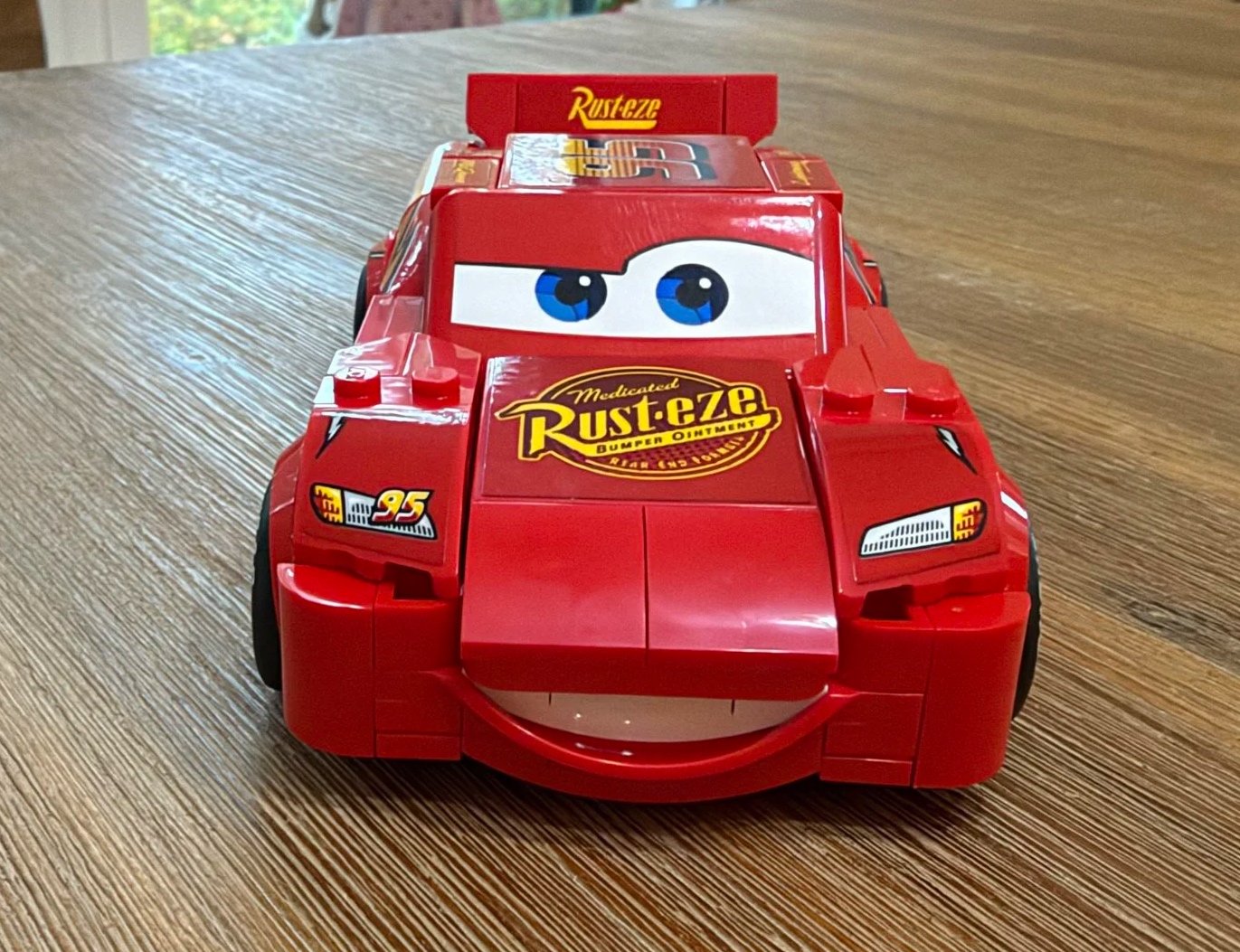 Front view of completed LEGO Lightning McQueen 77255 showing blue windshield eyes, a smiling bumper, and the Rust-eze hood logo.