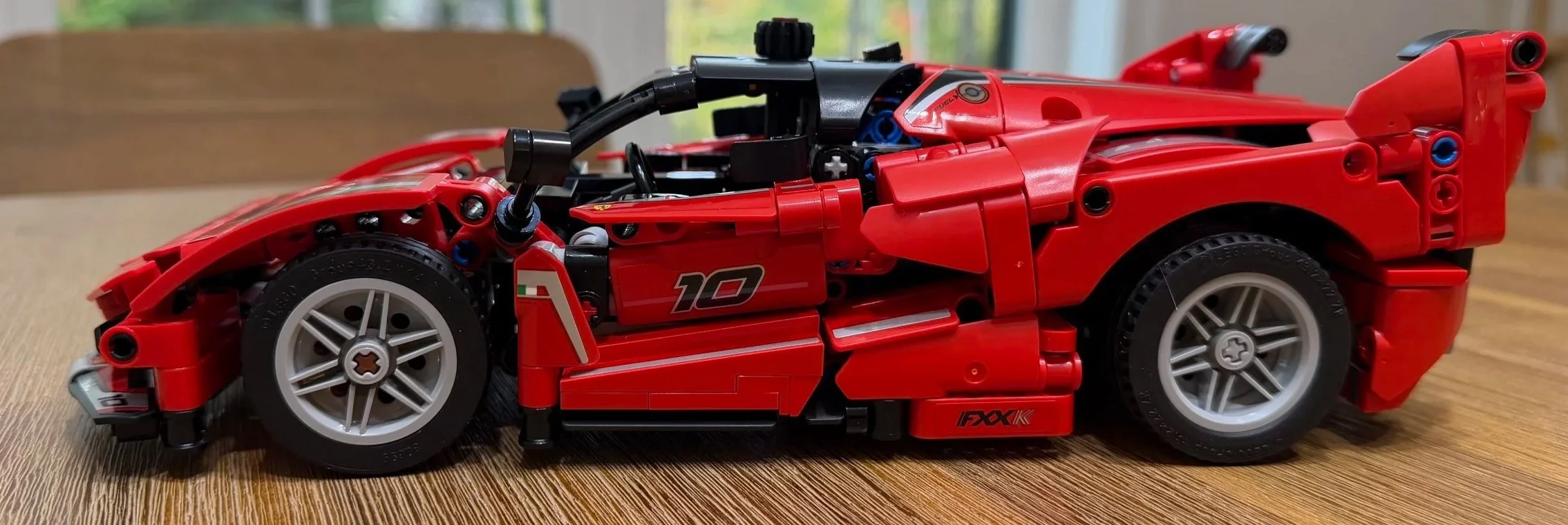 Side view of the completed LEGO Technic Ferrari FXX K 42212, with red bodywork, silver wheels, number 10 door graphic, and closed panels.