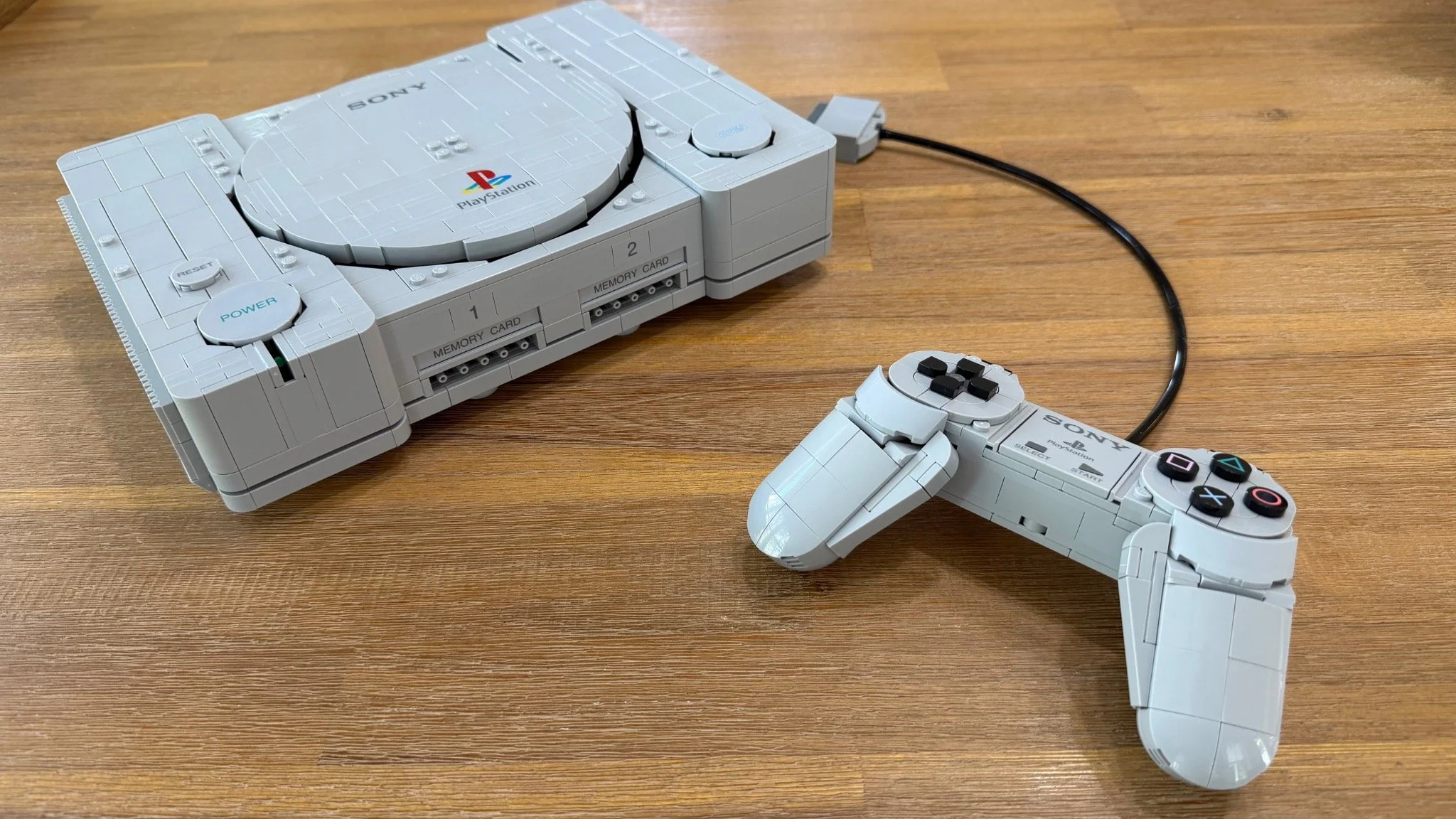Completed LEGO PlayStation 72306 console with its disc lid closed and original-style controller beside it on a wooden table.