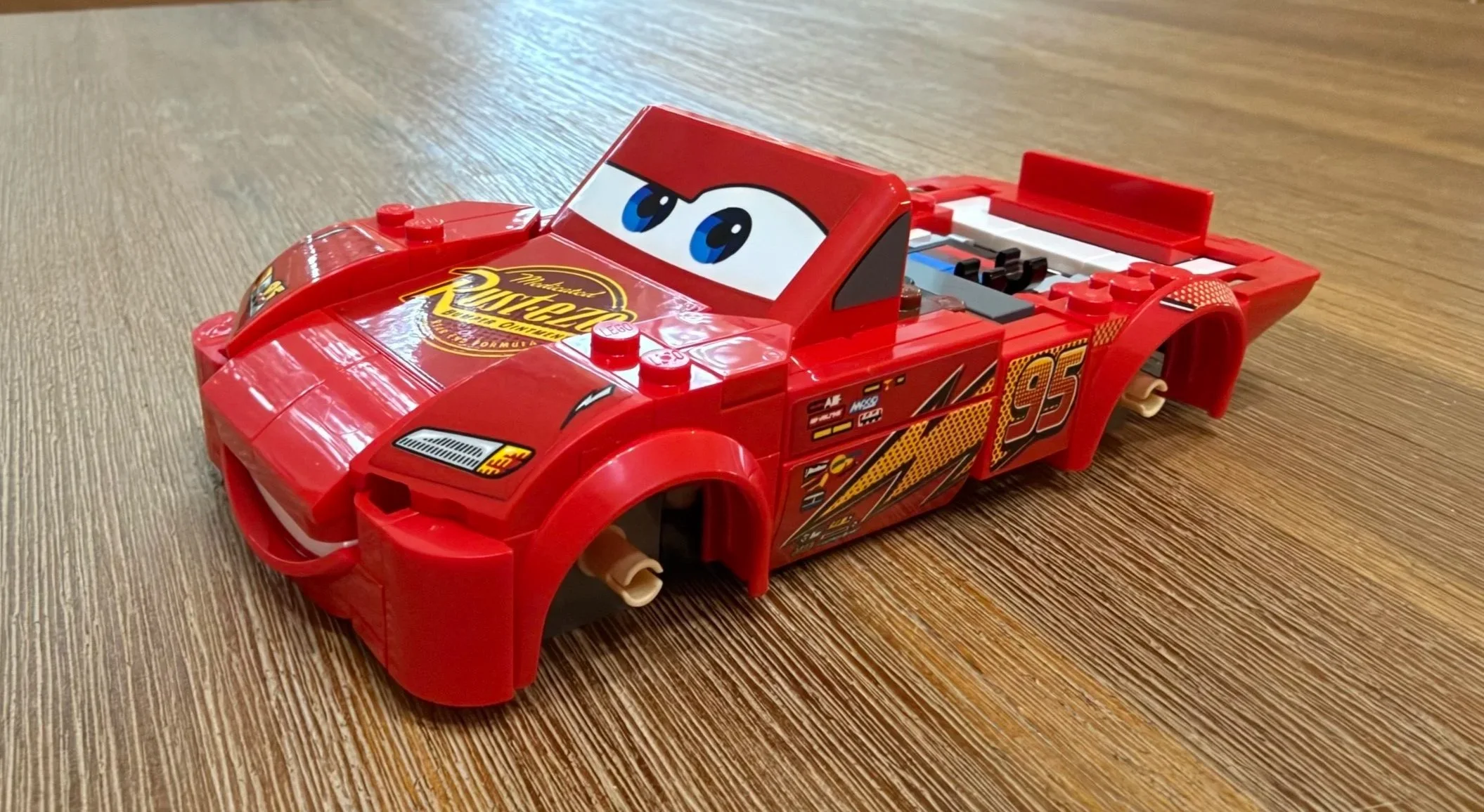 Unfinished LEGO Lightning McQueen with windshield eyes, Rust-eze hood logo, headlight decals, and open rear bodywork.