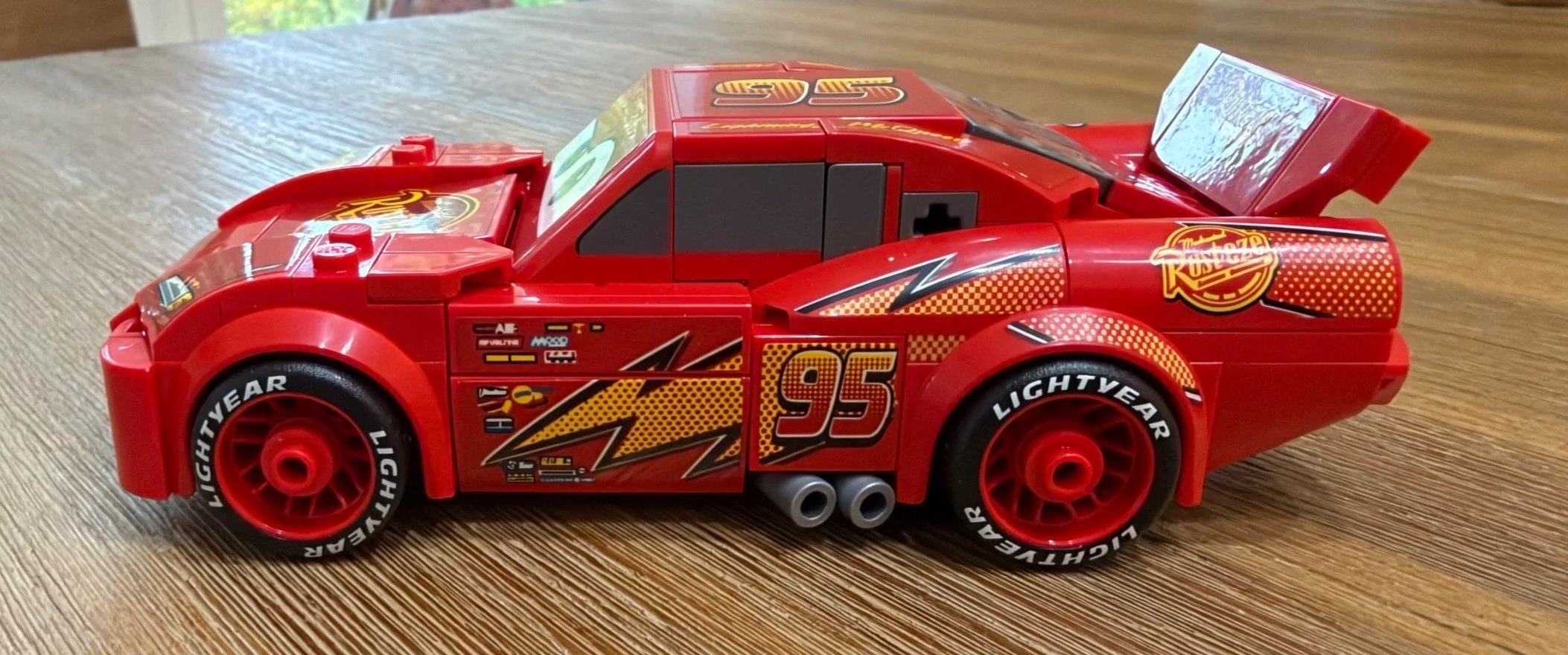 Side view of finished LEGO Lightning McQueen with number 95, lightning bolt graphics, Lightyear tires, and silver exhaust outlets.