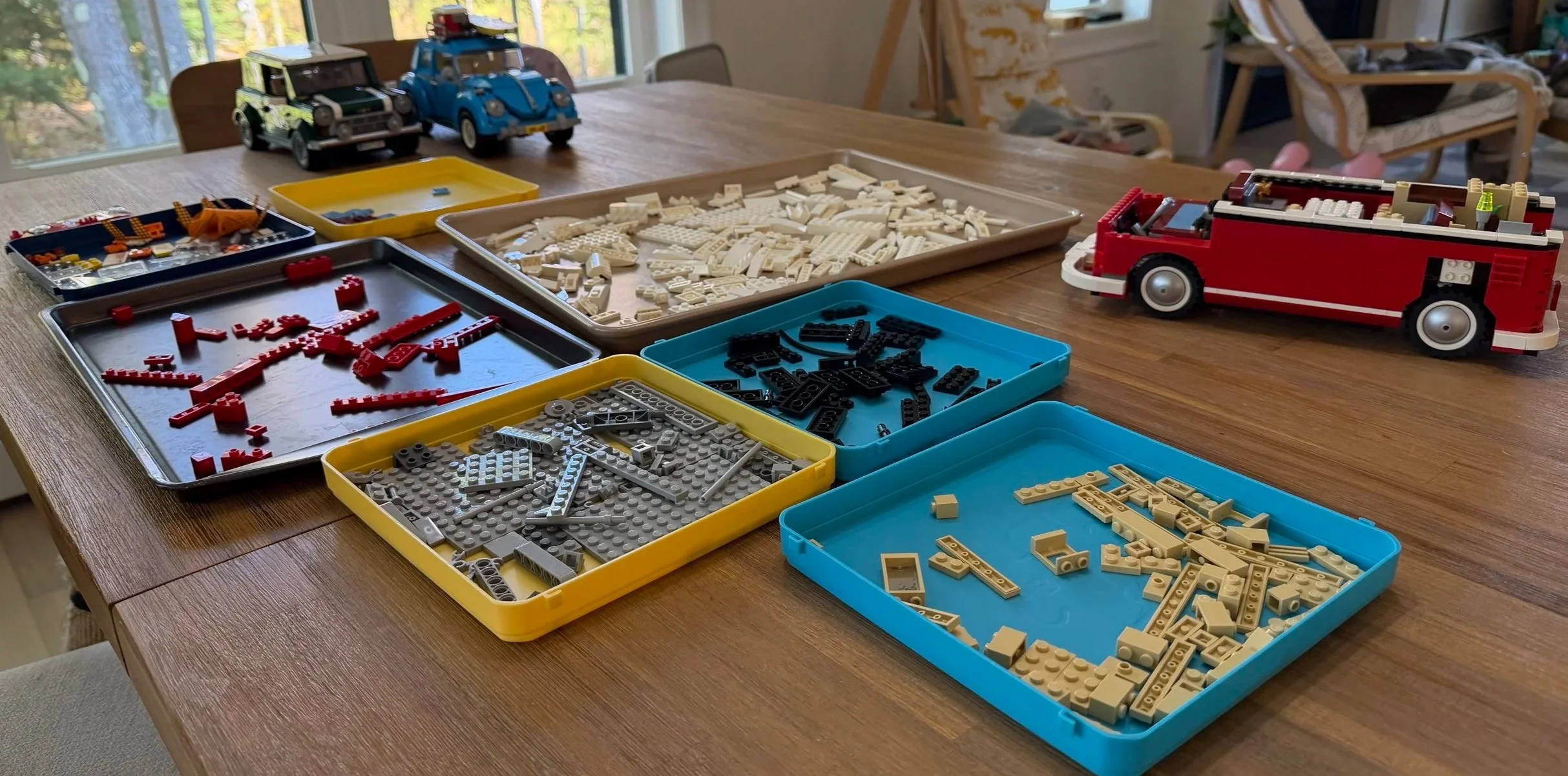 LEGO T1 Camper Van body with its roof removed beside sorted pieces, with the MINI Cooper and Beetle in the background.