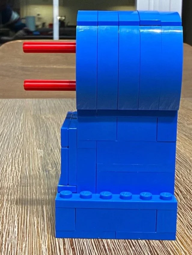 Side view of one blue brick-built LEGO Red leg with two red axles projecting from its rounded upper section.