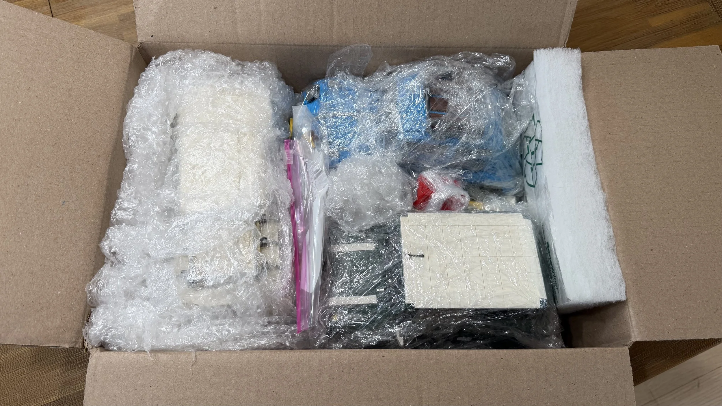 Wrapped LEGO vehicle models, a bag of loose pieces, bubble wrap and foam cushioning inside an open cardboard box.
