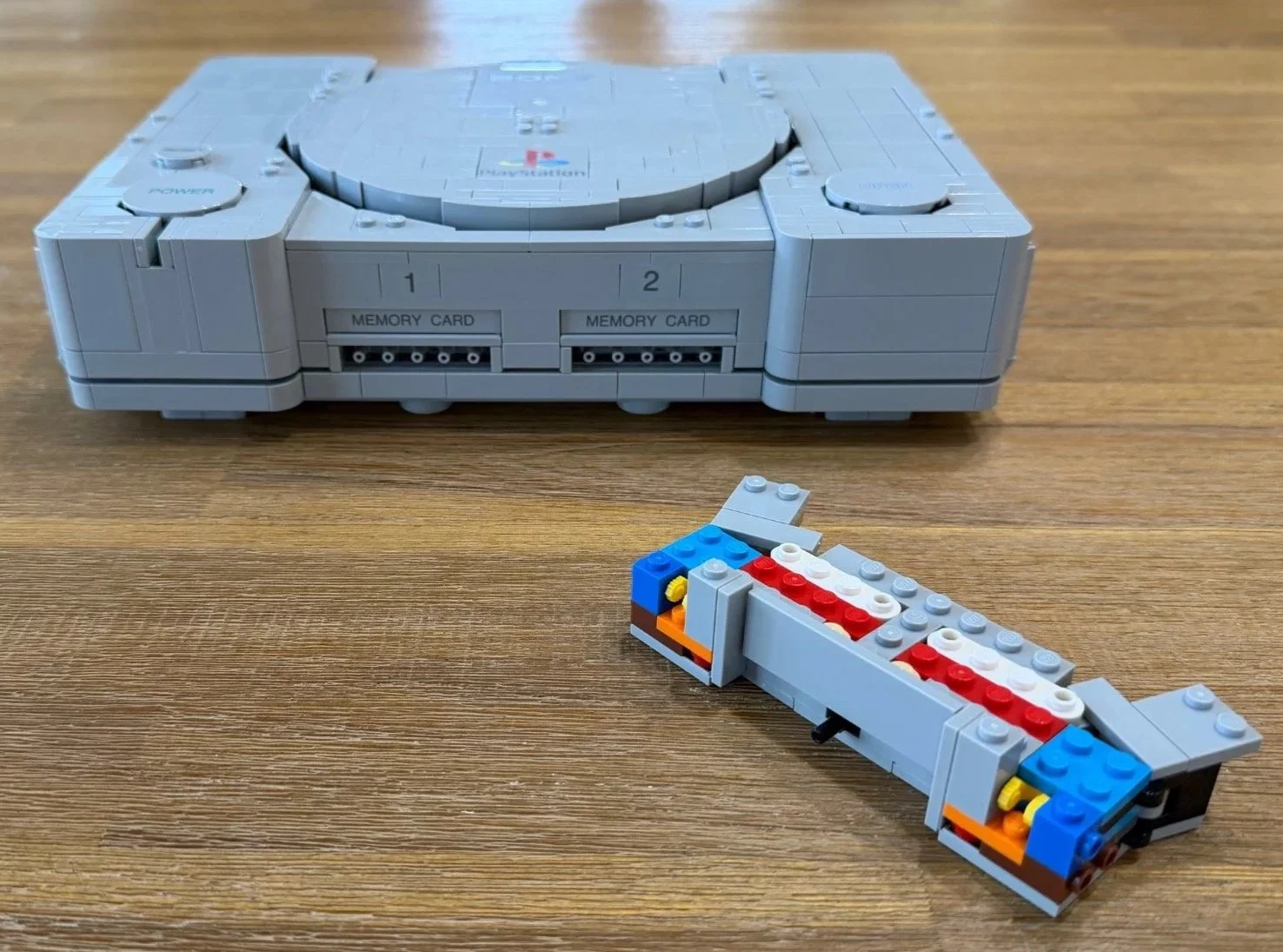 Partly built LEGO PlayStation controller base beside the completed console.