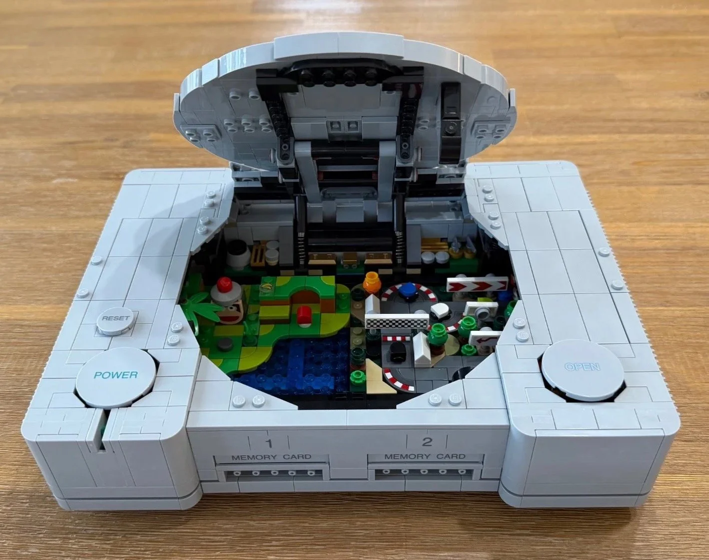 Completed LEGO PlayStation console with the disc lid open over its Ape Escape and Gran Turismo micro scenes.
