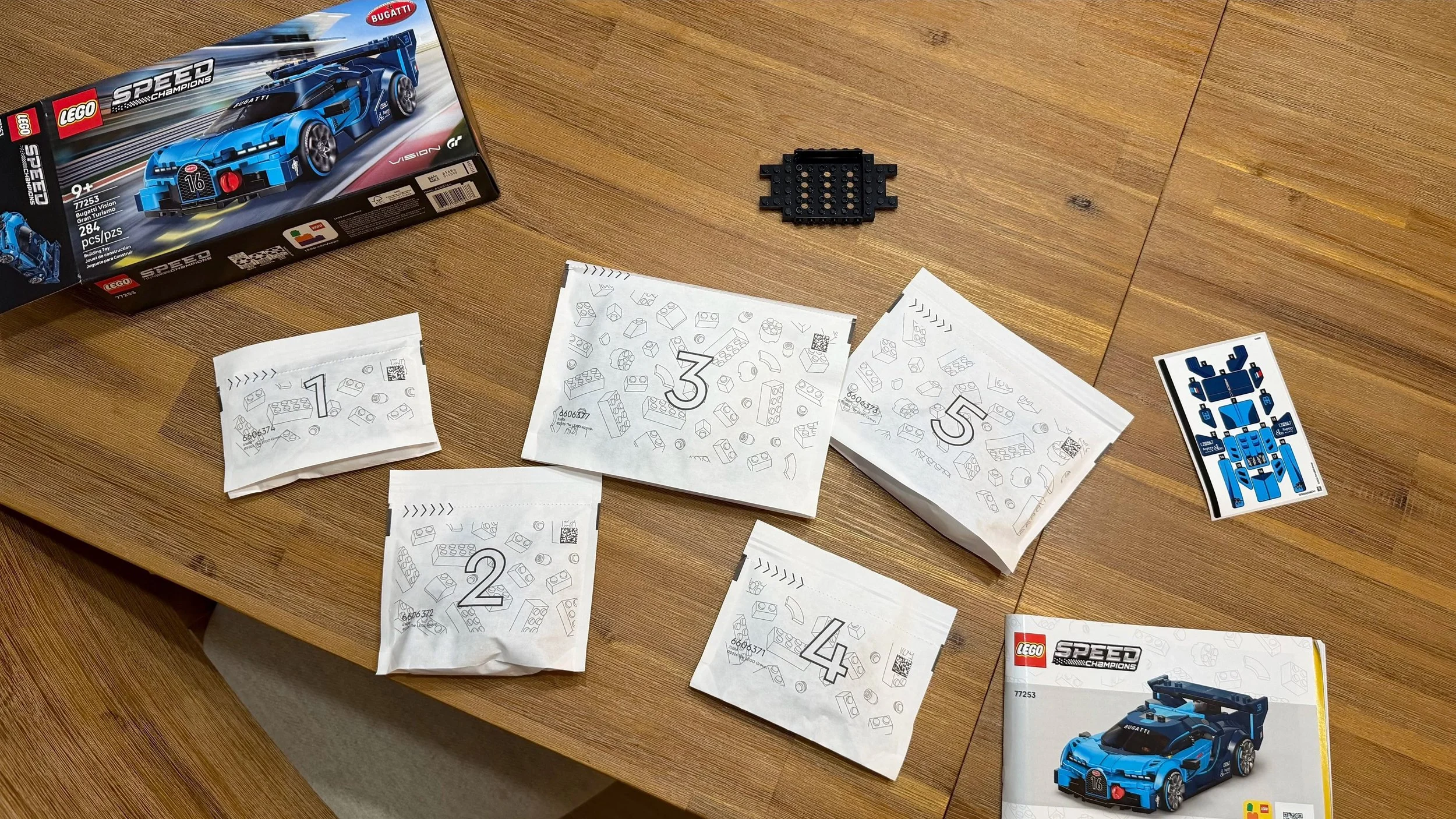 LEGO Bugatti 77253 box, five numbered bags, instructions, sticker sheet, and loose chassis on a wooden table.