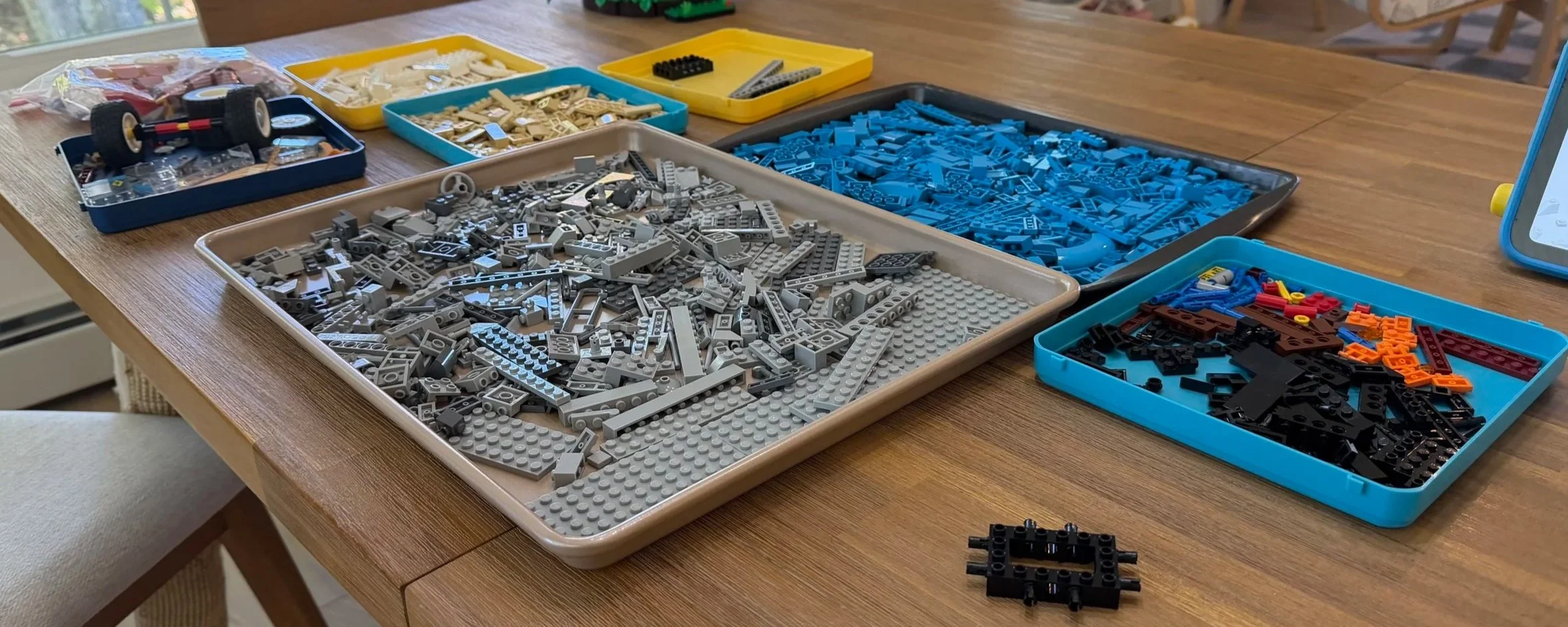 Blue, gray, tan, white and assorted LEGO pieces separated into trays on a table during the vehicle rebuild project.