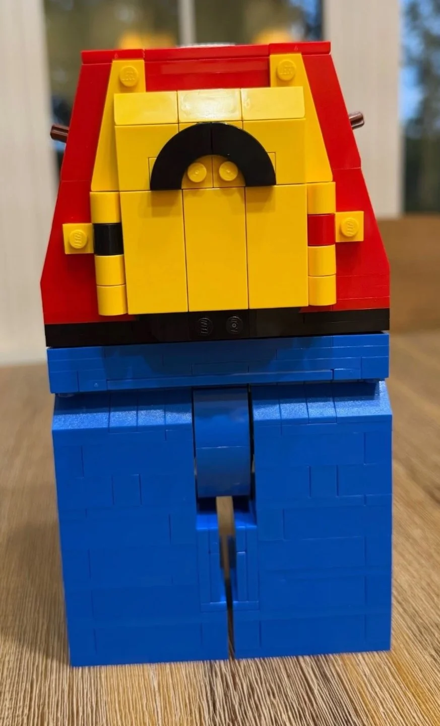 Rear of the headless LEGO Red figure, showing a yellow brick-built backpack with a black handle above blue legs.