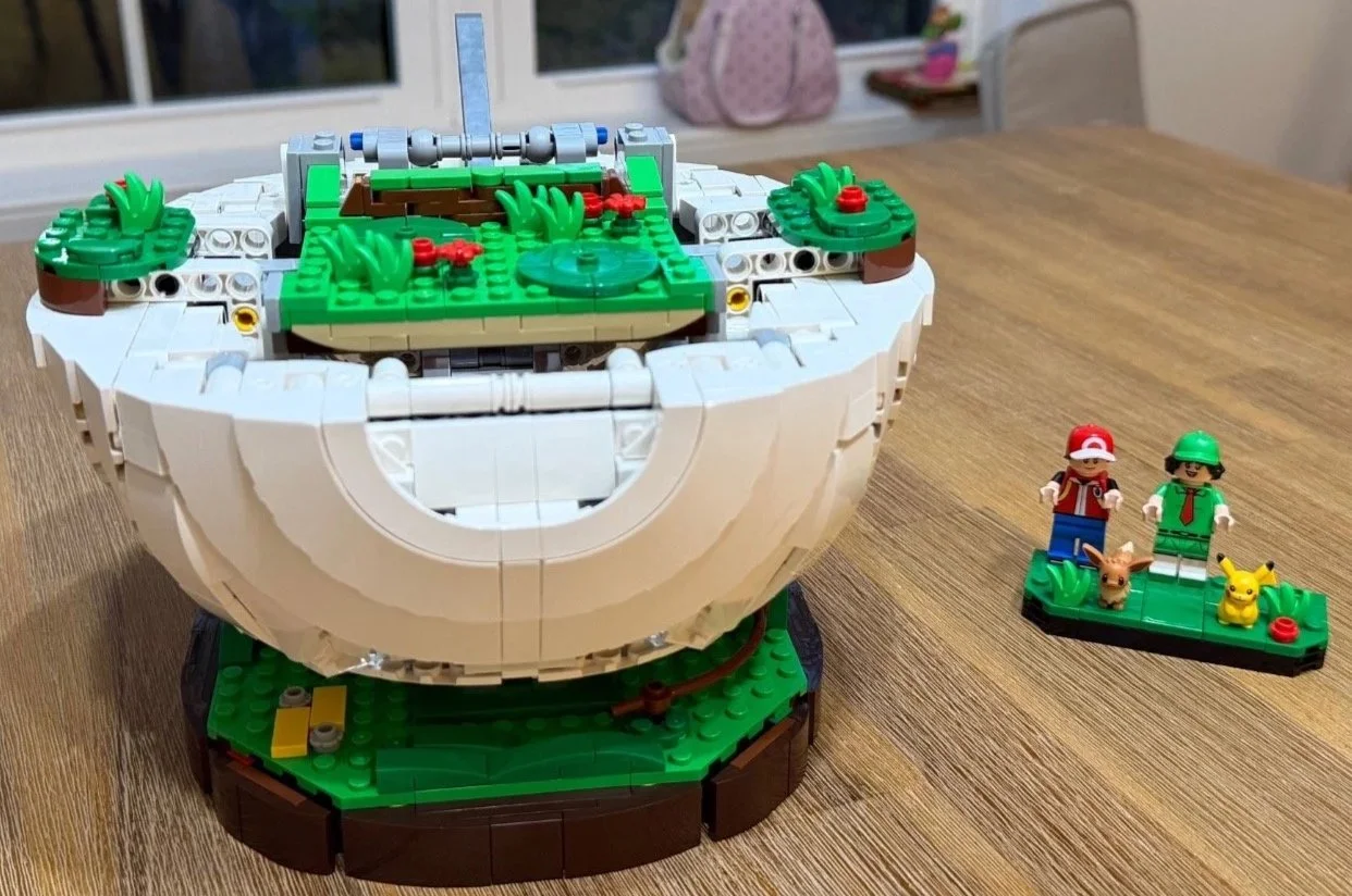 White lower Poké Ball shell around the green battle platform, with character figures beside the model.