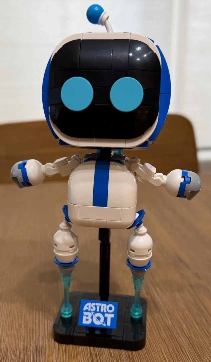 Completed LEGO Astro Bot 40899 with round blue eyes, white body and propulsion effects above its labeled stand.
