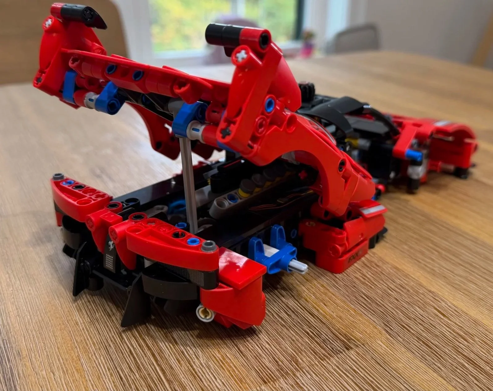 Unfinished Ferrari FXX K with its large red engine cover raised on a support above the exposed engine, before wheels and doors are added.