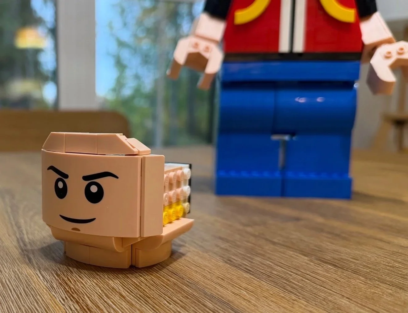 Partly built LEGO Red head with its decorated face in sharp focus on the table and the headless body blurred behind it.