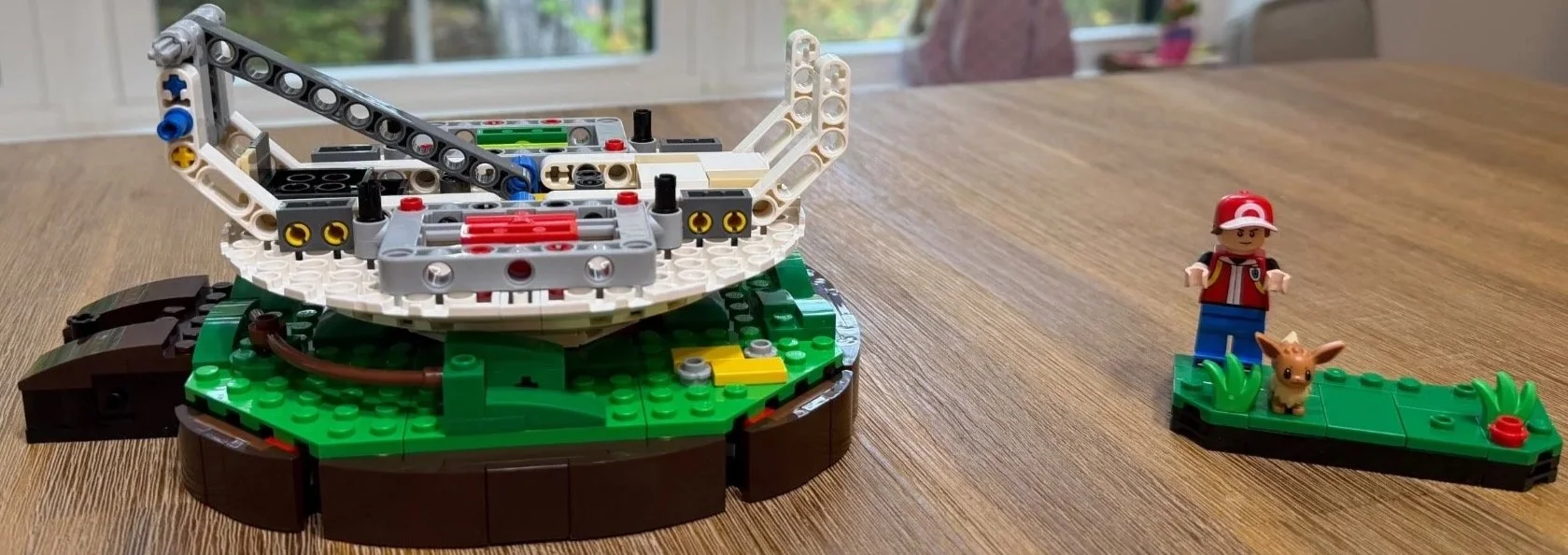 Early LEGO Poké Ball Technic frame mounted on the base with Red and Eevee beside it.