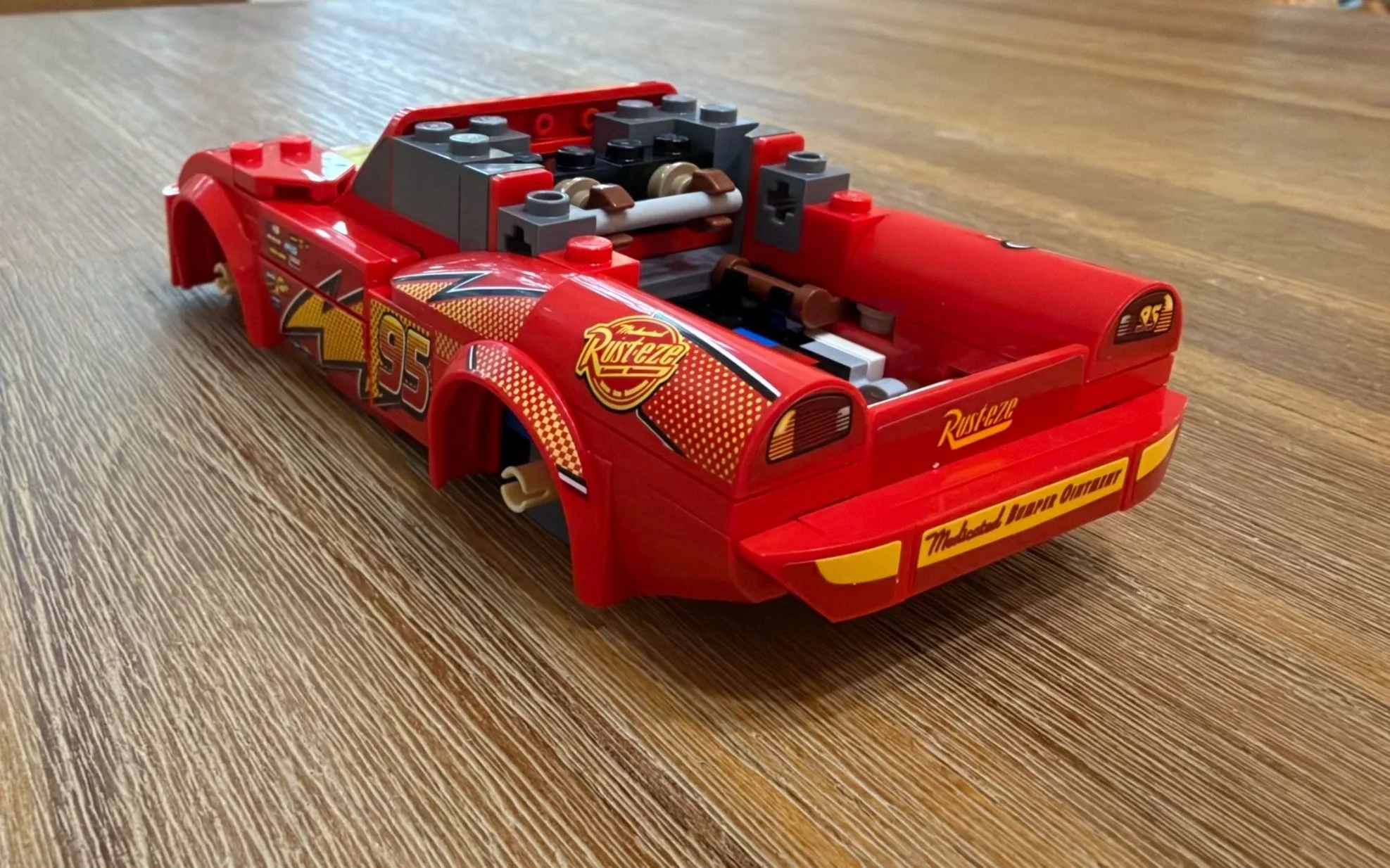 Rear three-quarter view of unfinished LEGO Lightning McQueen showing taillights, decorated rear panels, and exposed internal structure.
