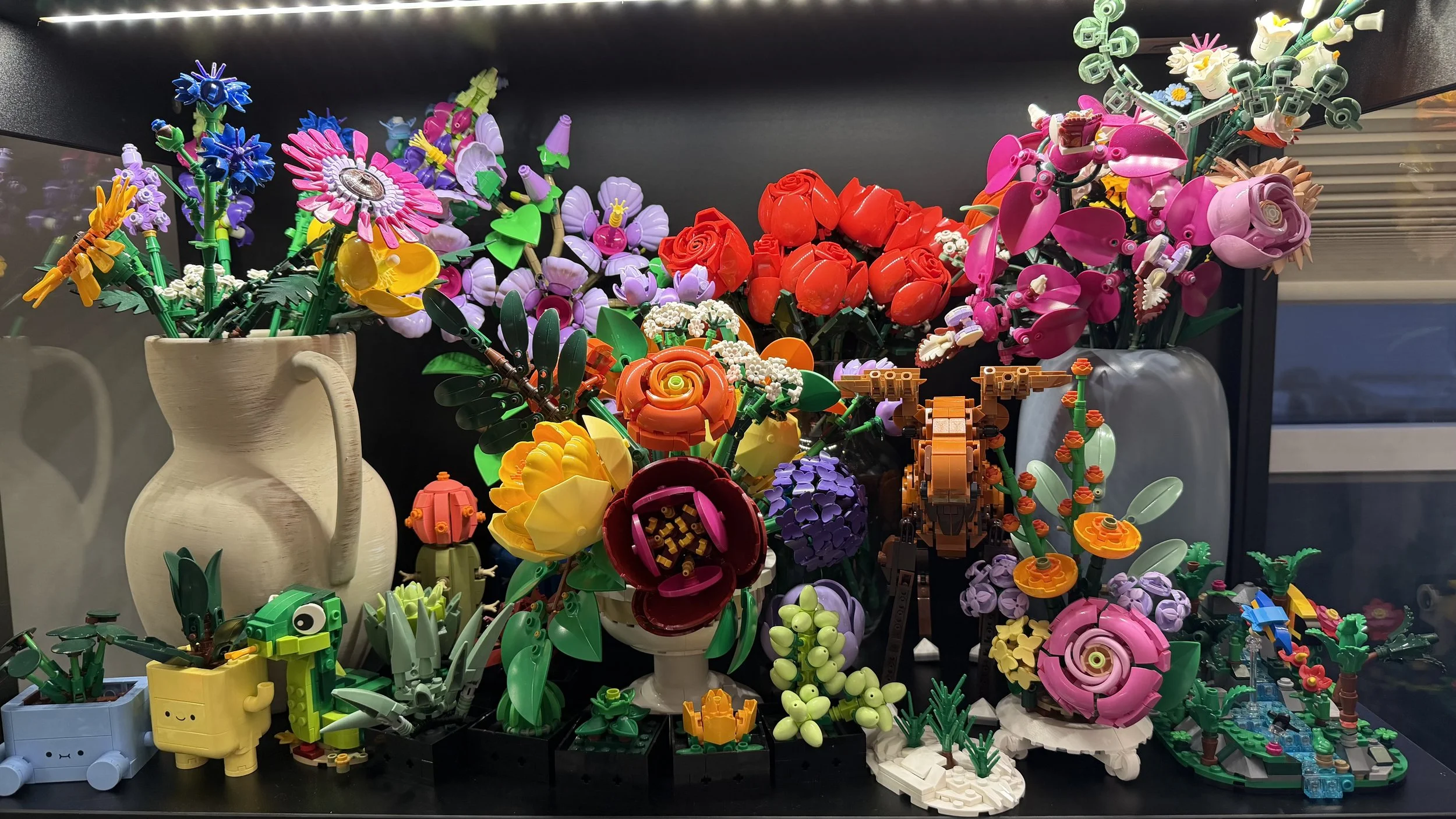 Colorful Lego flower arrangements in vases and planters, including roses, orchids, and other flowers, on display on a black surface.