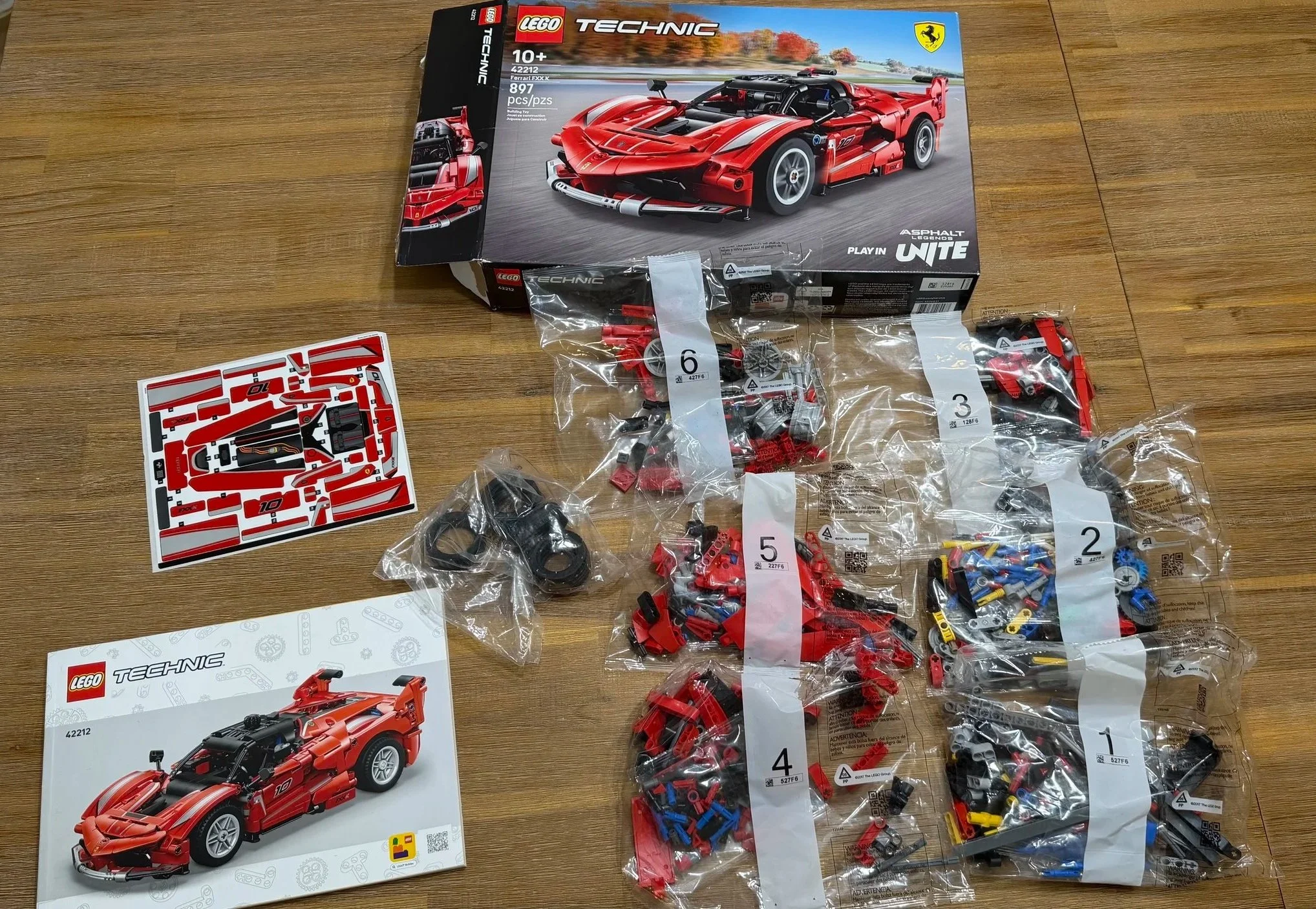 LEGO Technic Ferrari FXX K 42212 box, instruction booklet, six numbered bags, tires, and sticker sheet on a wooden table.