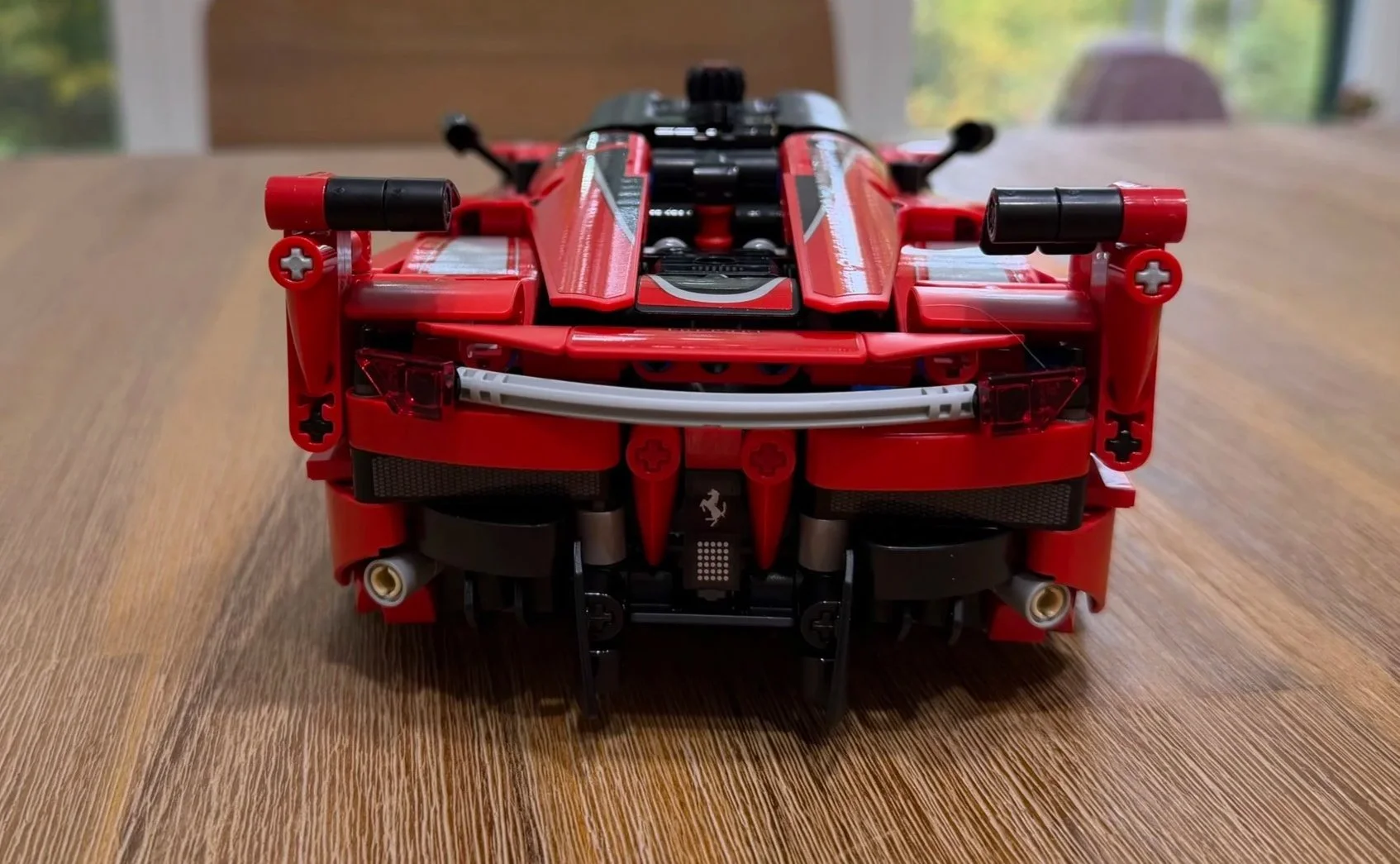 Rear view of the completed Ferrari FXX K showing raised wing tips, red taillights, twin exhaust outlets, and a black lower diffuser.