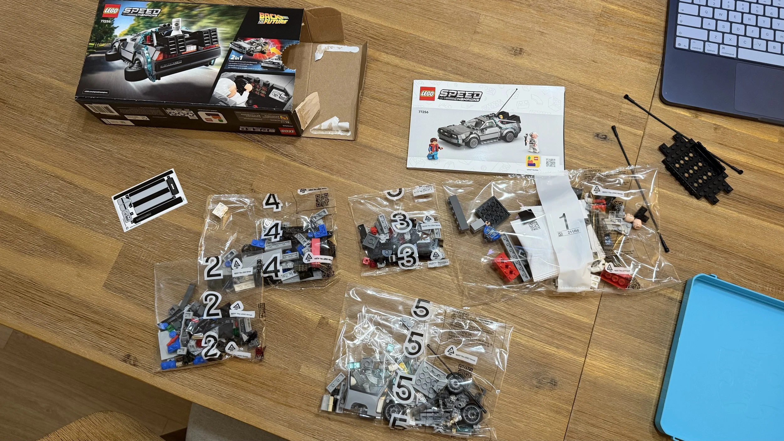 LEGO 77256 box, five numbered bags, instructions, sticker sheet, and loose chassis pieces on a wooden table.