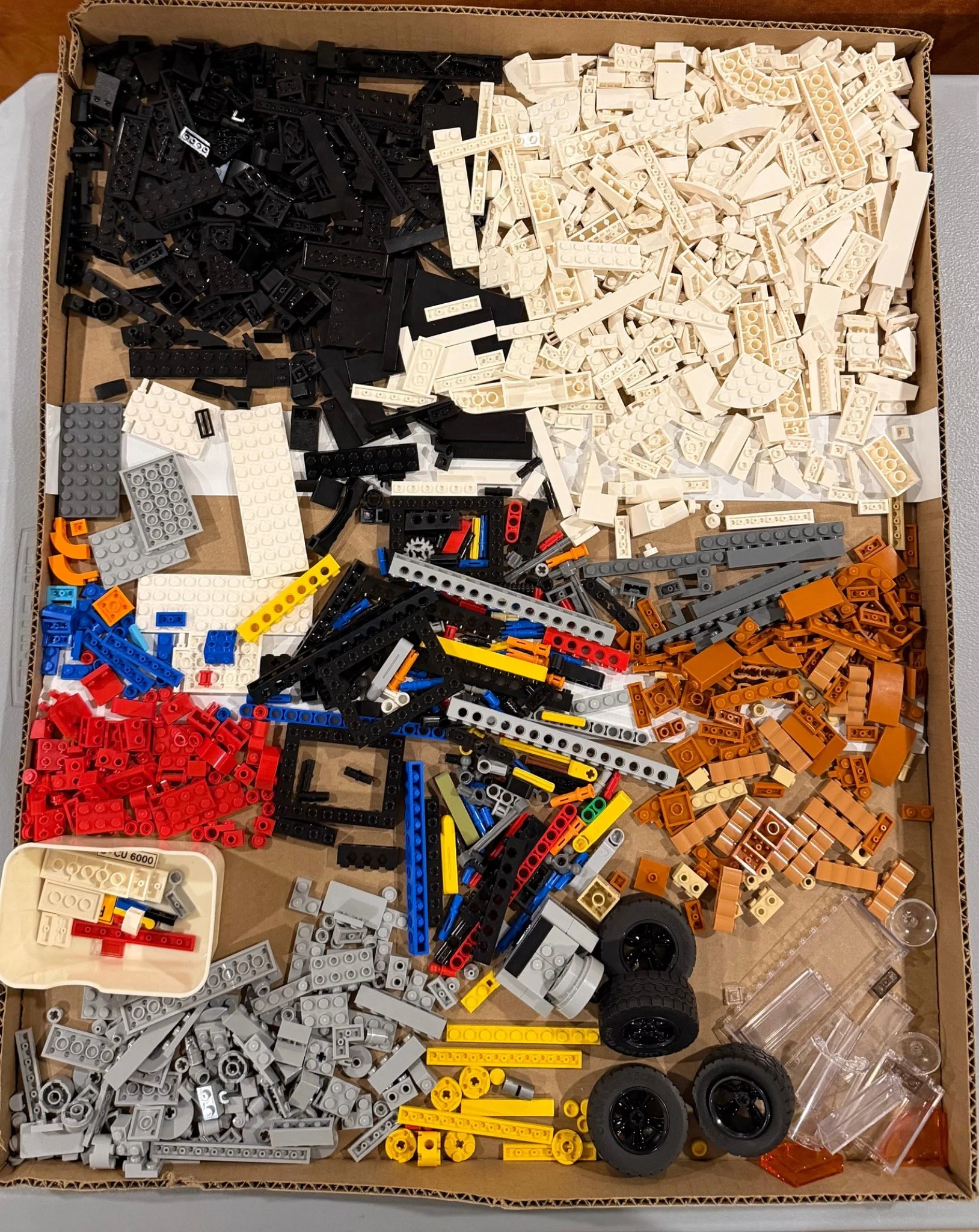 LEGO Porsche pieces grouped mainly by color in a large cardboard tray before reassembly.
