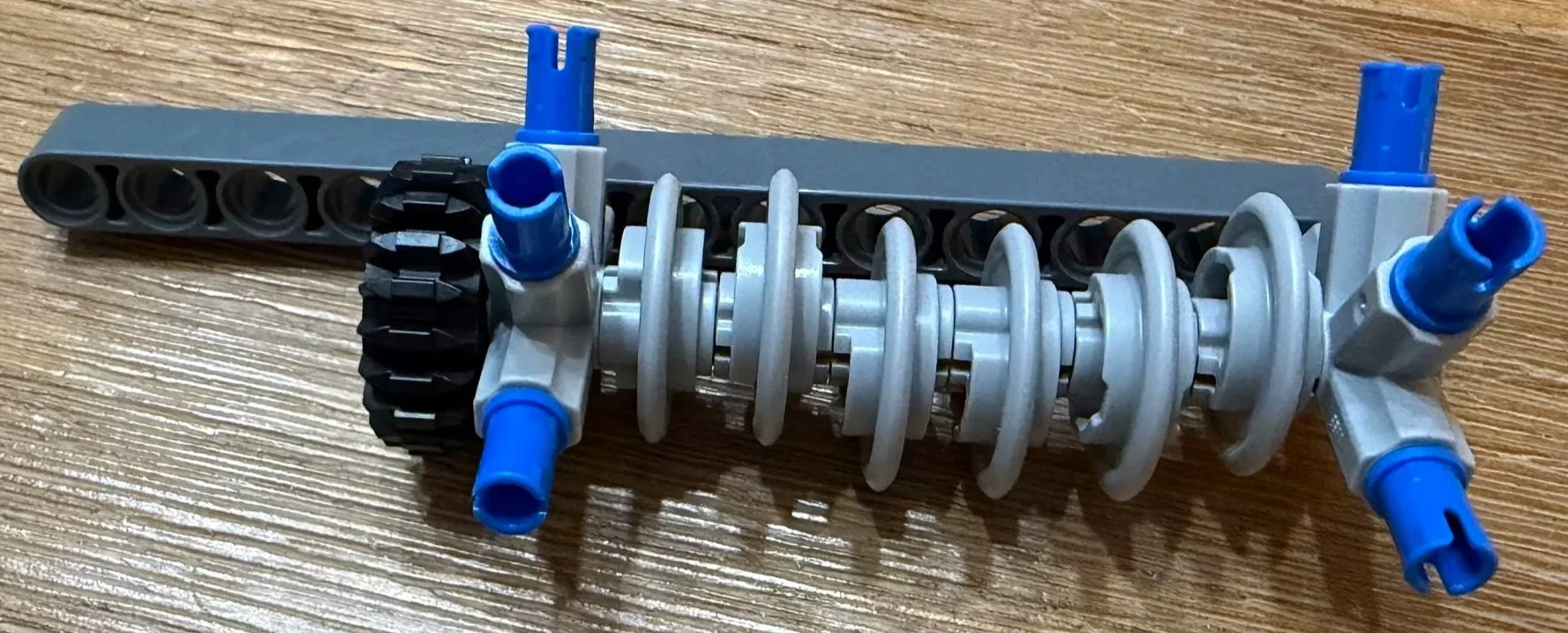 Close-up of the Ferrari FXX K crankshaft subassembly, showing gray offset pieces on an axle beside a black gear and blue pins.